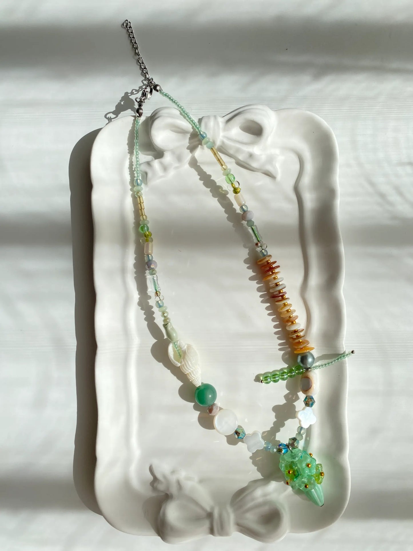 Poetic view of the 1-of-1 green floral necklace resting on a ceramic plate, capturing a soft and gentle aesthetic.