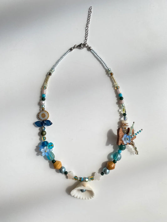 Flat lay of HuibenCraft 1-of-1 necklace with coconut puppy, Czech glass sunflowers, and genuine shell pendant on a white table.