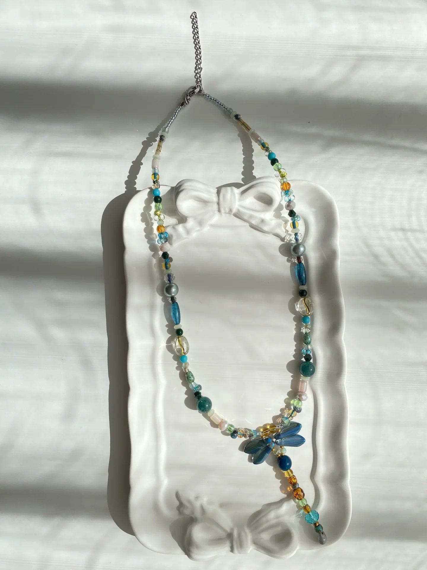 Poetic view of the 1-of-1 blue dragonfly necklace resting on a ceramic plate, capturing a playful and whimsical aesthetic.