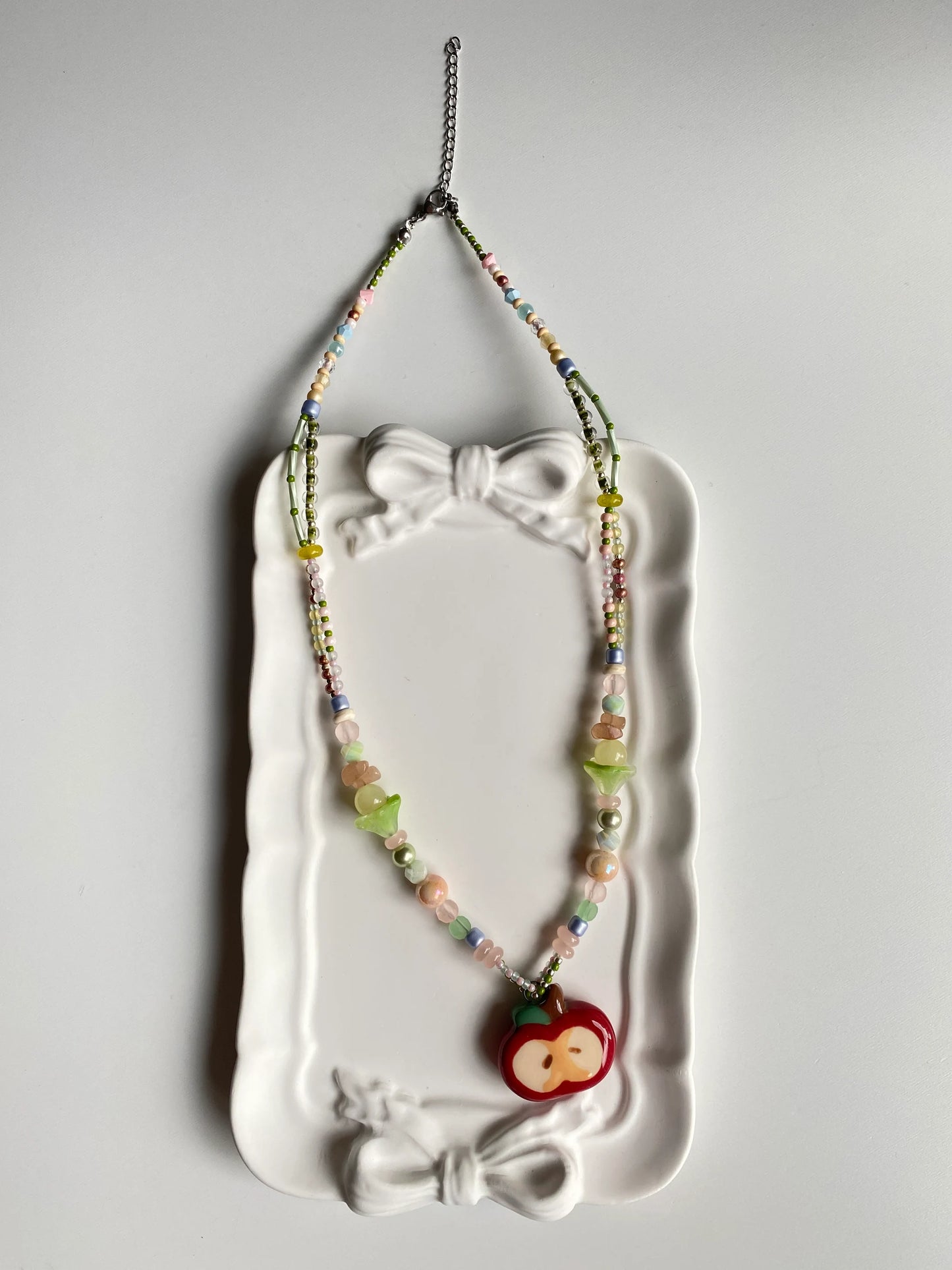 Close-up of an artisan beaded necklace with a ceramic apple pendant displayed in a decorative dish.