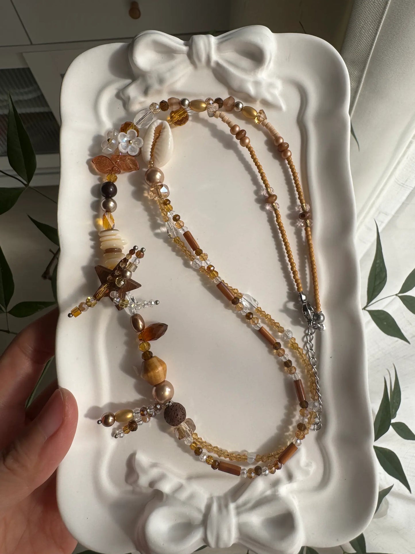 HuibenCraft 1-of-1 bohemian-style layered necklace with shimmering khaki beads and floral details, placed in a white ceramic dish.