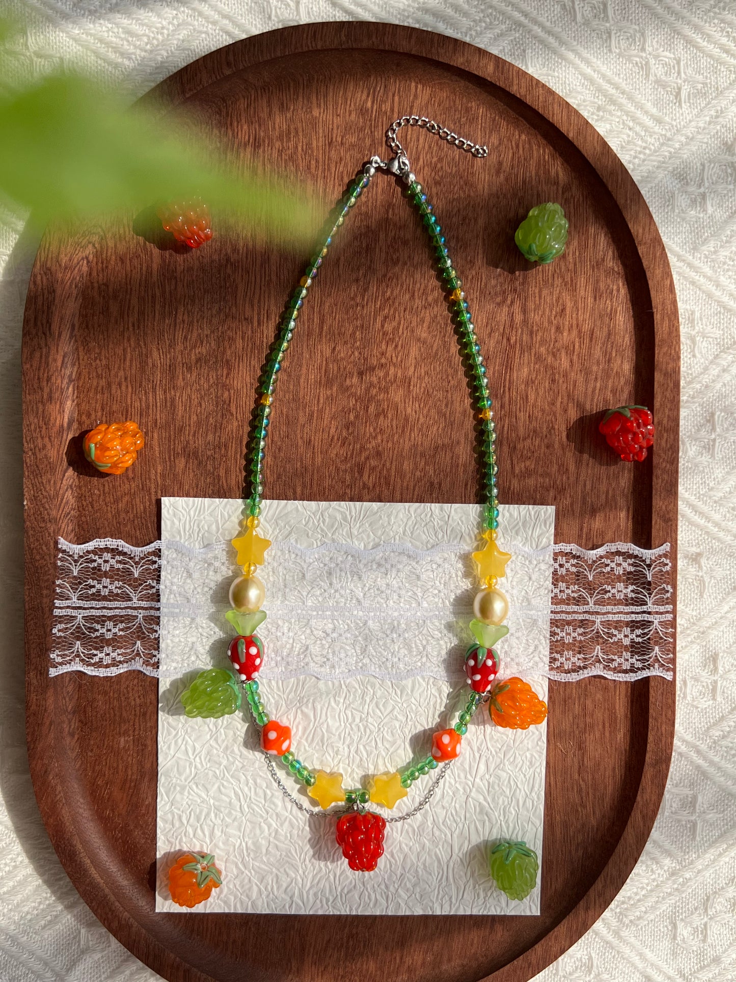Whimsical Raspberry Strawberry Necklace arranged on a wooden tray with raspberry beads nearby.