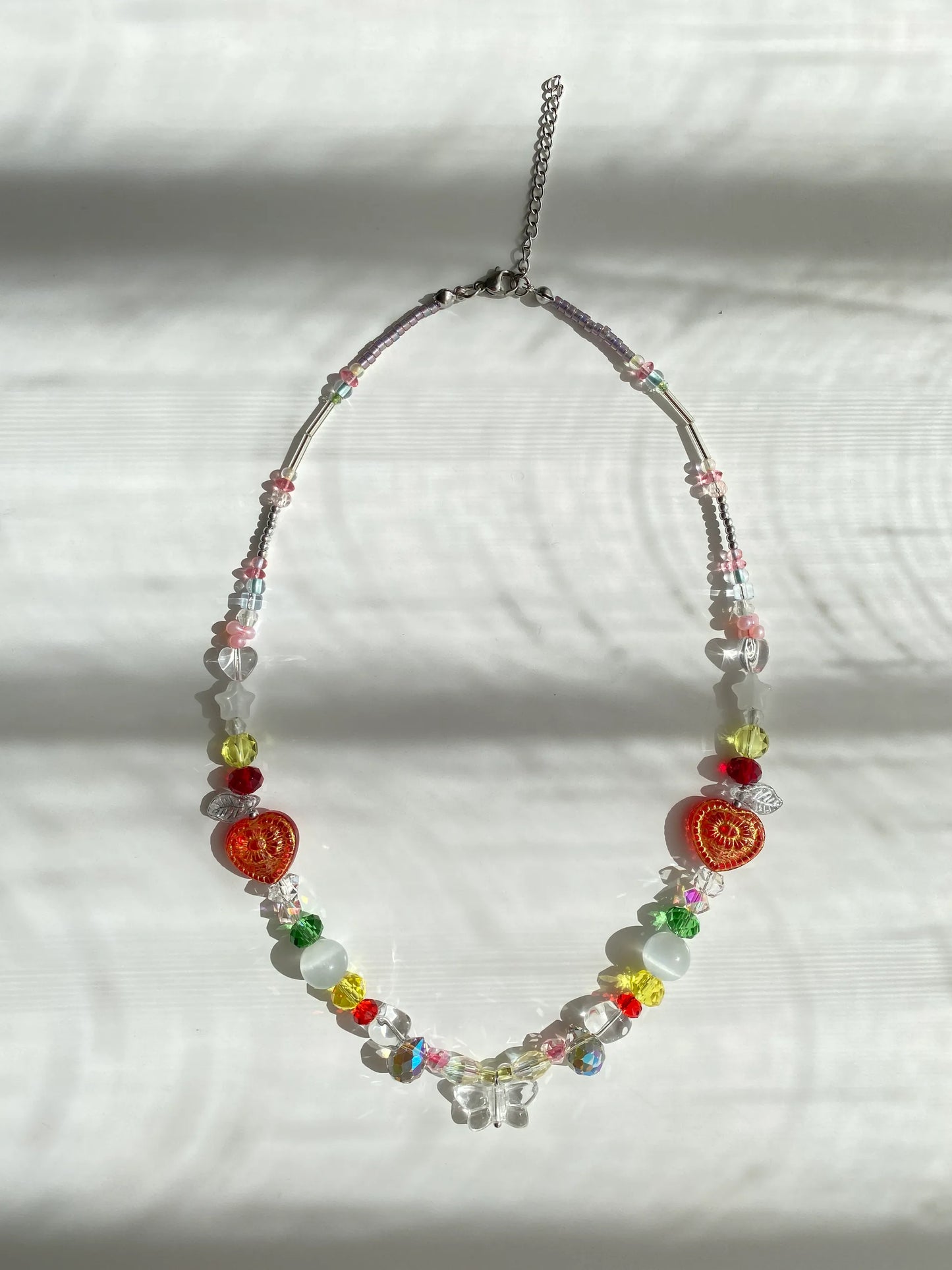 Colorful artisan seed bead necklace with a white butterfly pendant and wired cat's eye beads, flat lay on a table highlighting its vibrant summer aesthetic.
