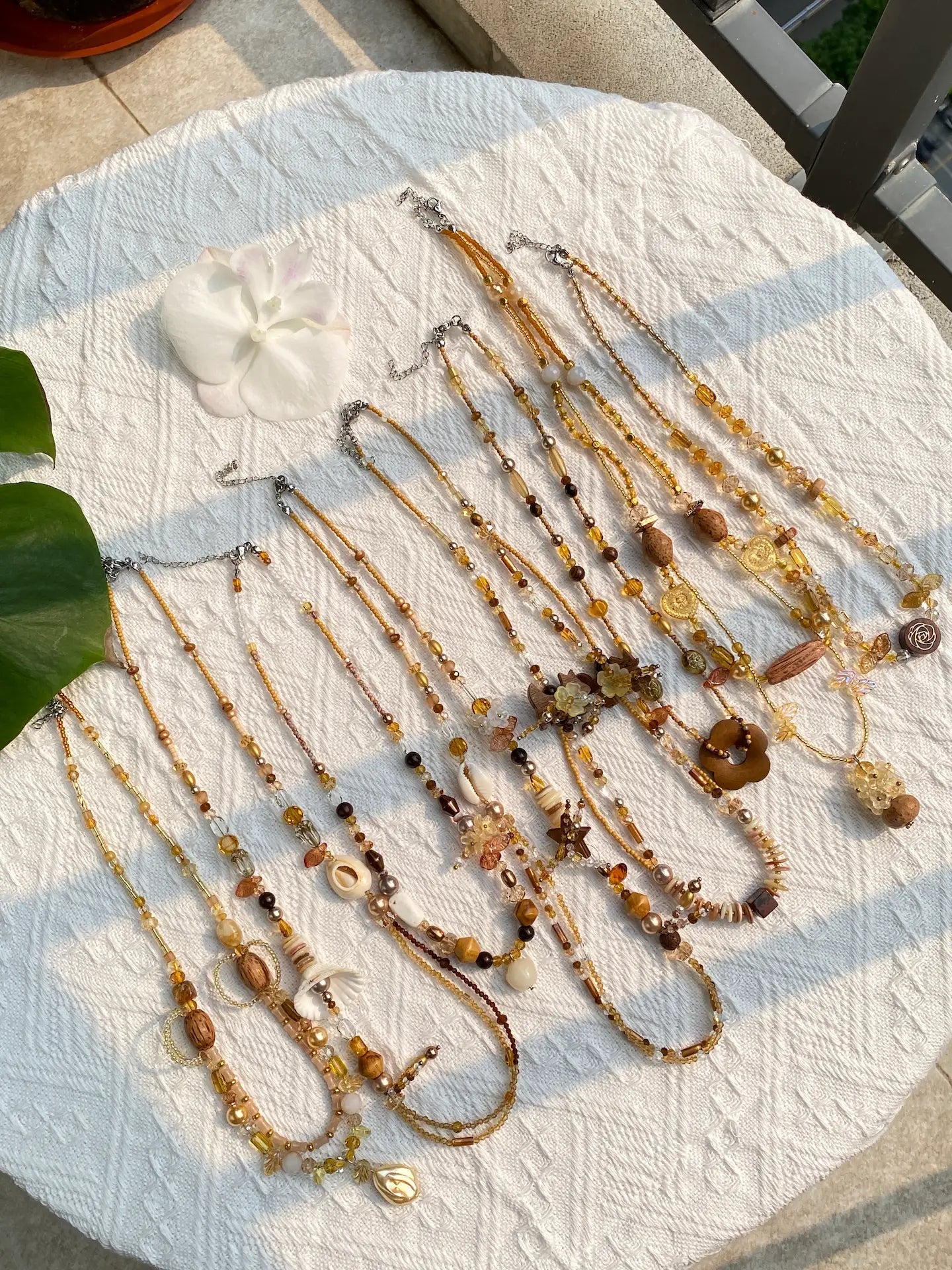 A luxurious flat lay of 10 HuibenCraft 1-of-1 earthy brown and amber necklaces featuring wooden beads and shimmering crystals, captured in golden sunlight.
