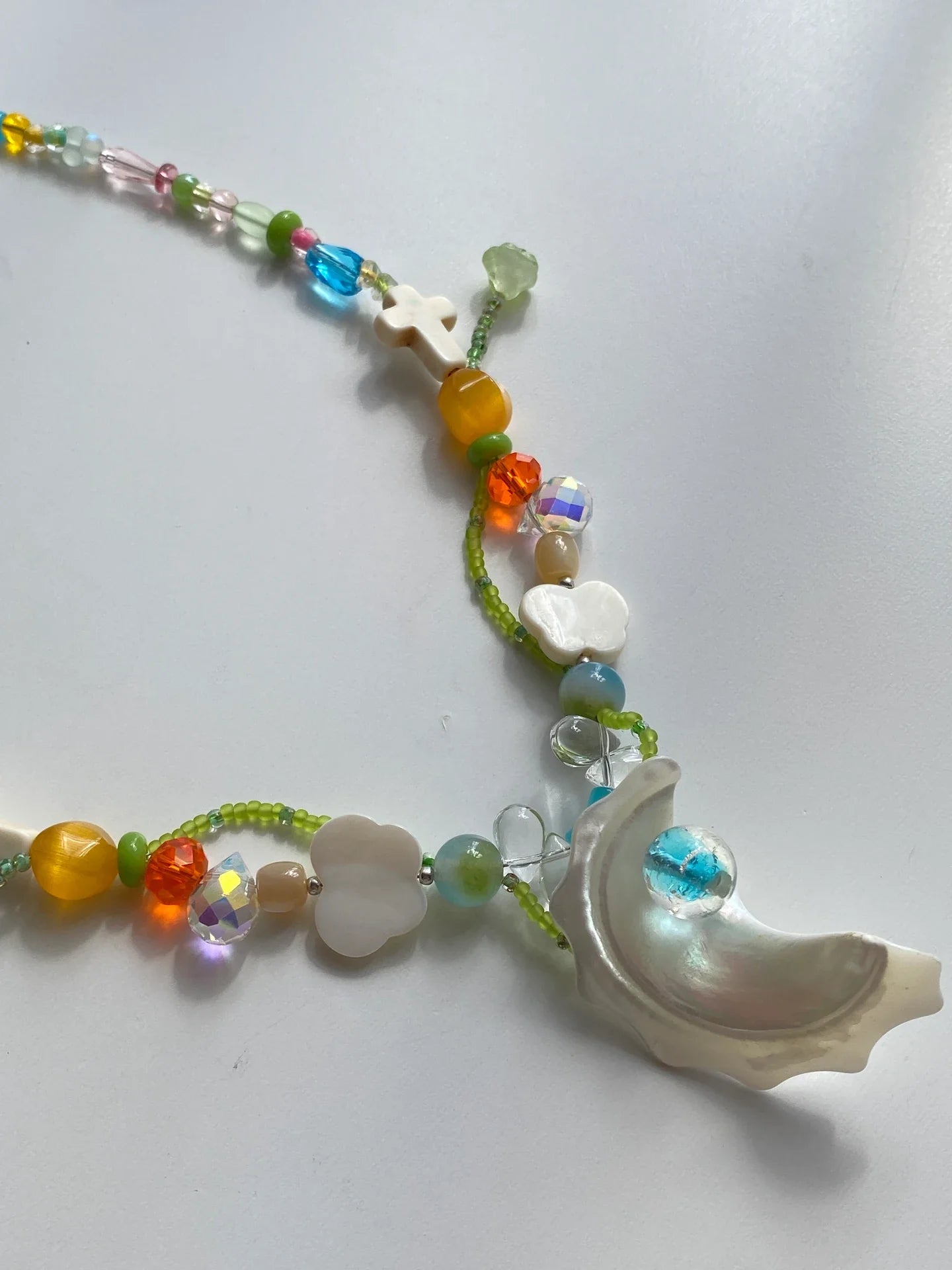 A close-up of HuibenCraft's new arrival necklace featuring a Trochus shell pendant with a blue glass pearl, butterfly shells, and orange cat-eye glass beads.
