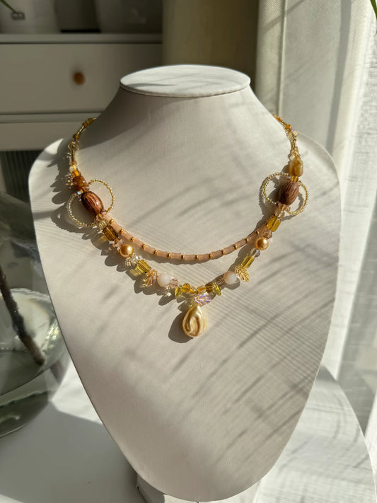 A 1-of-1 double-layered beaded necklace with bamboo-shaped beads and a yellow baroque pear-shaped glass pendant on a jewelry bust.