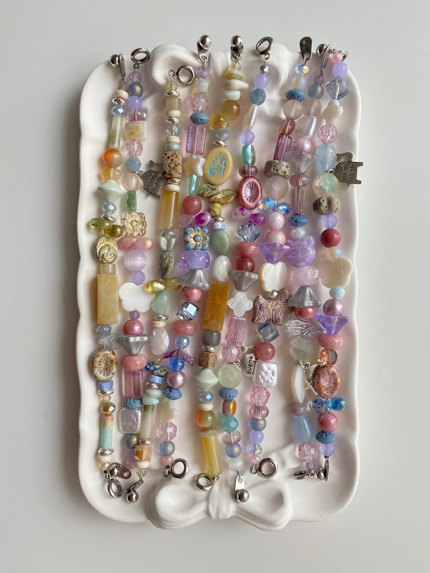 Flat lay of 9 unique HuibenCraft botanical garden bracelets with Czech glass and shells on a plate.