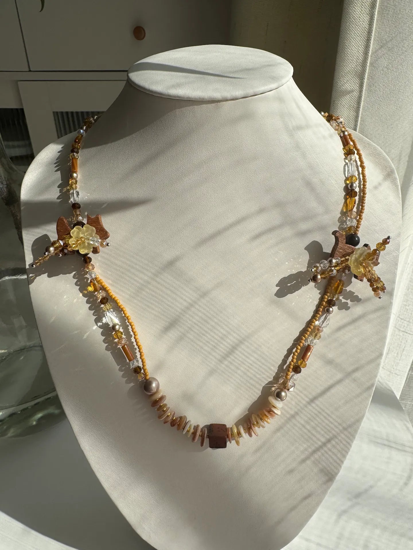 A 1-of-1 double-layered beaded necklace featuring handcrafted cat and dog coconut shell buttons with floral details, displayed on a jewelry bust.