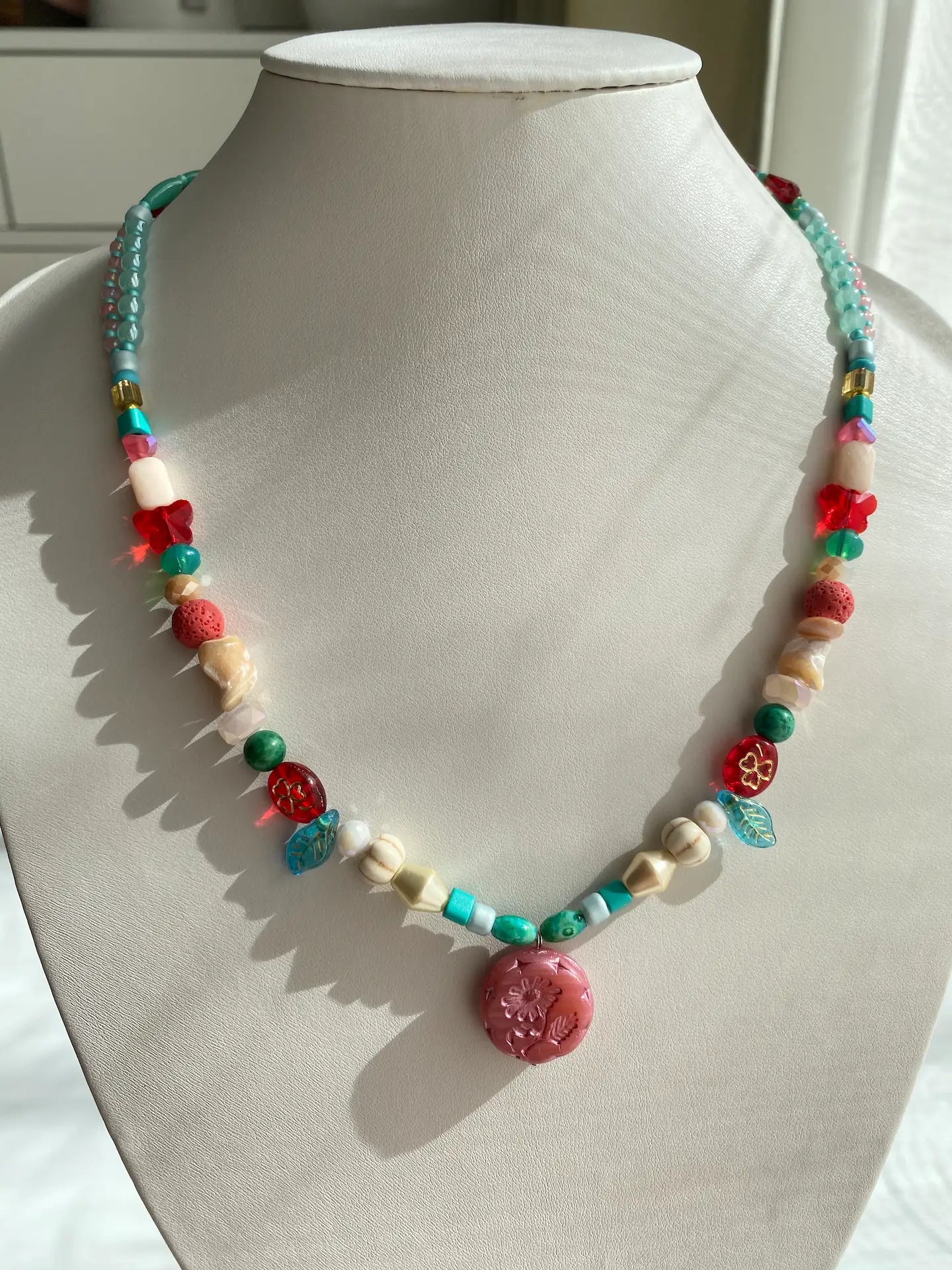 A 1-of-1 nostalgic layered necklace in pink, red, and blue with a pink Czech glass Marguerite pendant on a jewelry bust.