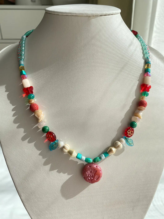 A 1-of-1 nostalgic layered necklace in pink, red, and blue with a pink Czech glass Marguerite pendant on a jewelry bust.