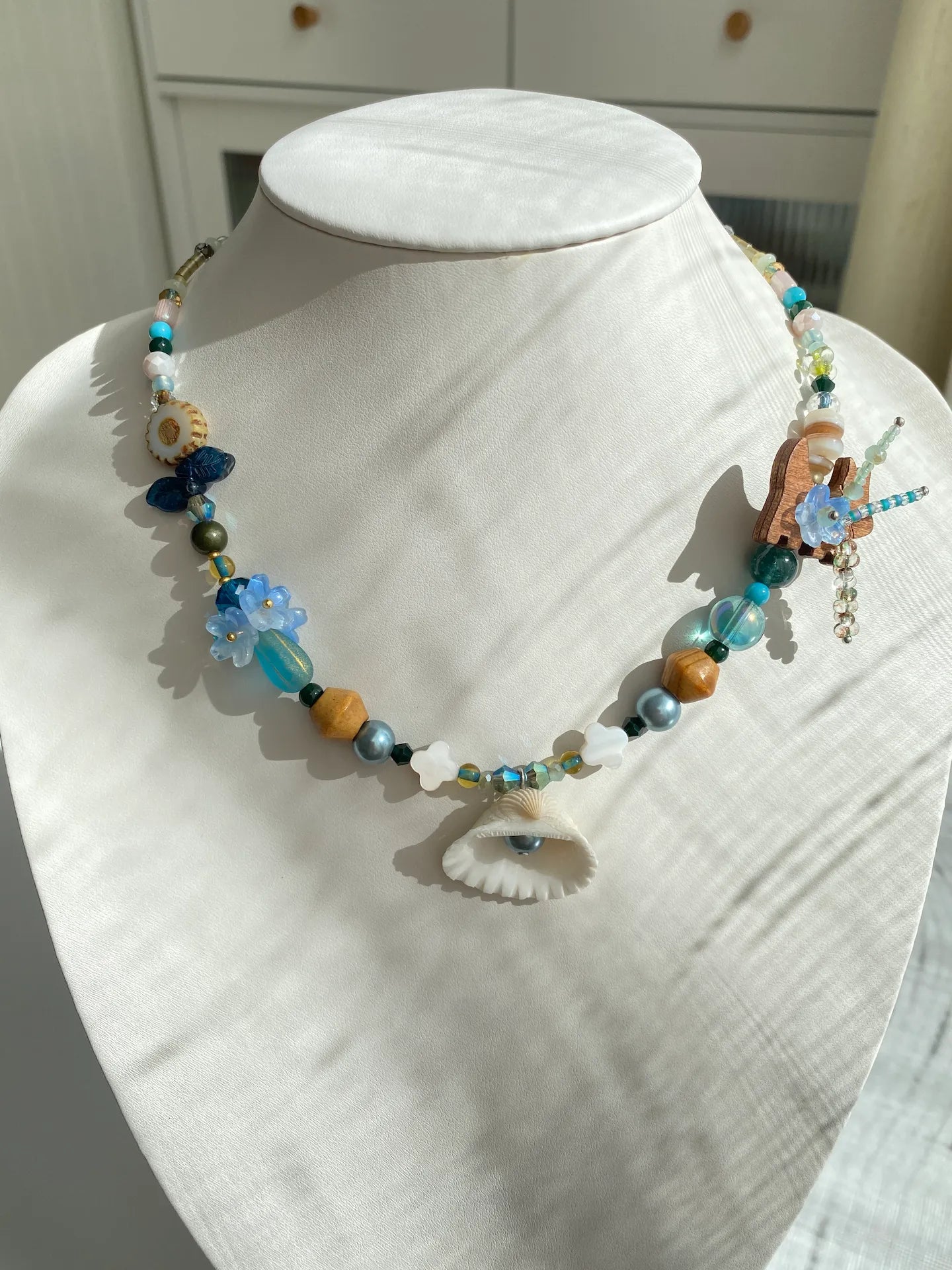 Handcrafted 1-of-1 shell necklace featuring a whimsical coconut puppy and floral beads worn on a mannequin neck.