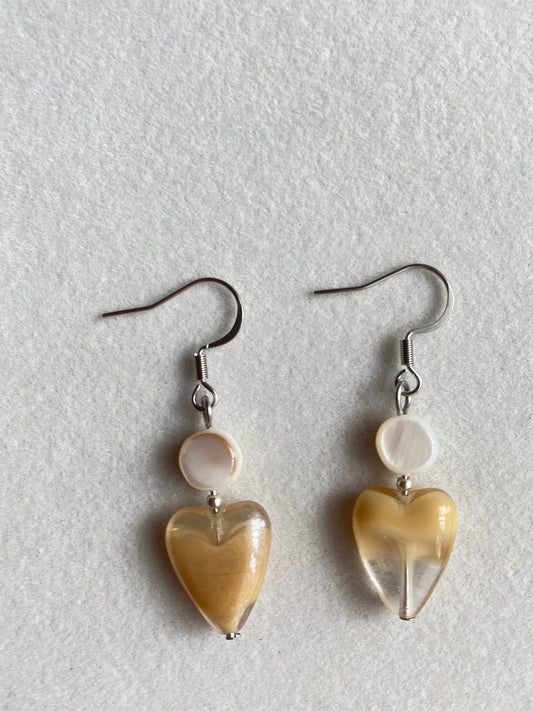 A 1-of-1 pair of cute latte-colored Czech glass heart earrings with natural round shell charms on a white tablecloth.