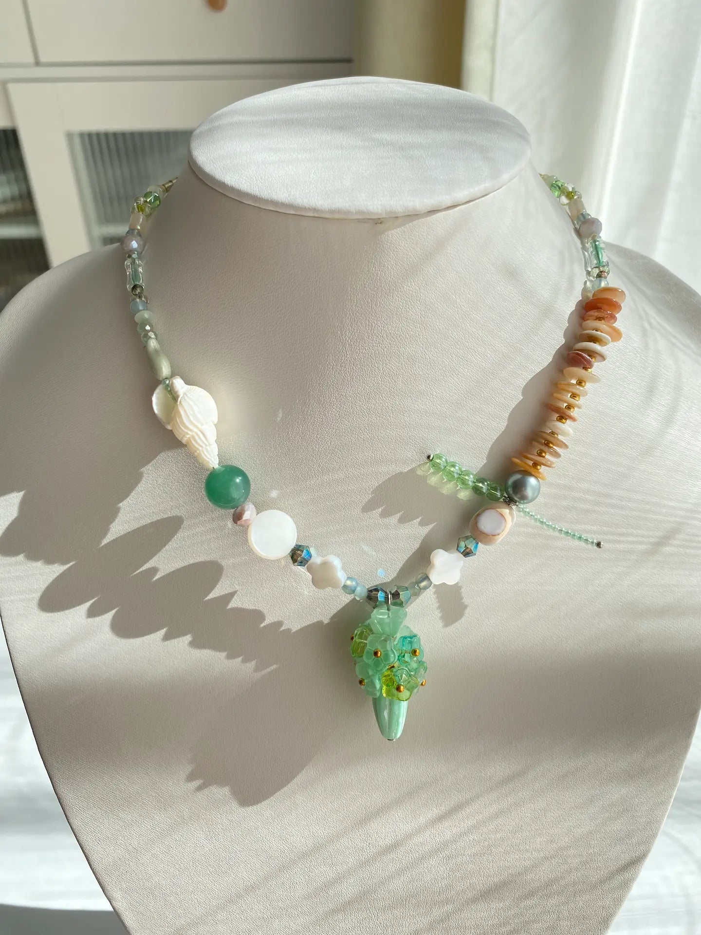 Handcrafted 1-of-1 floral necklace featuring a Czech glass vase pendant and shell accents worn on a mannequin neck.
