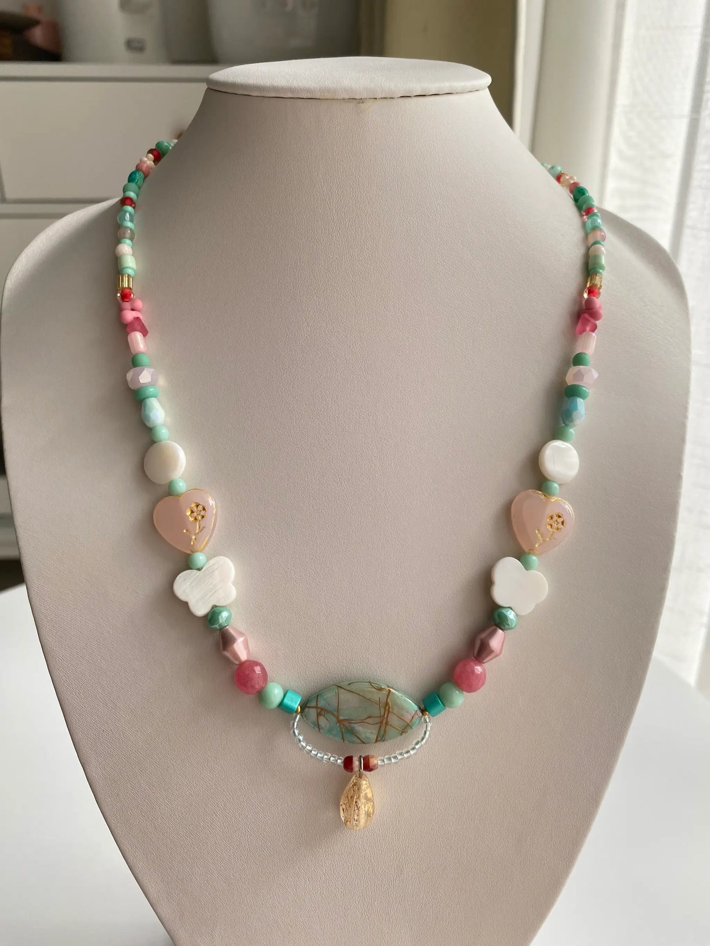 A 1-of-1 nostalgic layered necklace in pink, red, and blue with a pink Czech glass Marguerite pendant on a jewelry bust.
