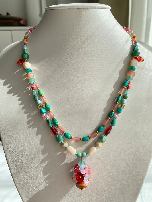A 1-of-1 ethnic-style double-layered necklace in pine blue and crimson red with a heavy-workmanship ceramic floral vase pendant on a jewelry bust.
