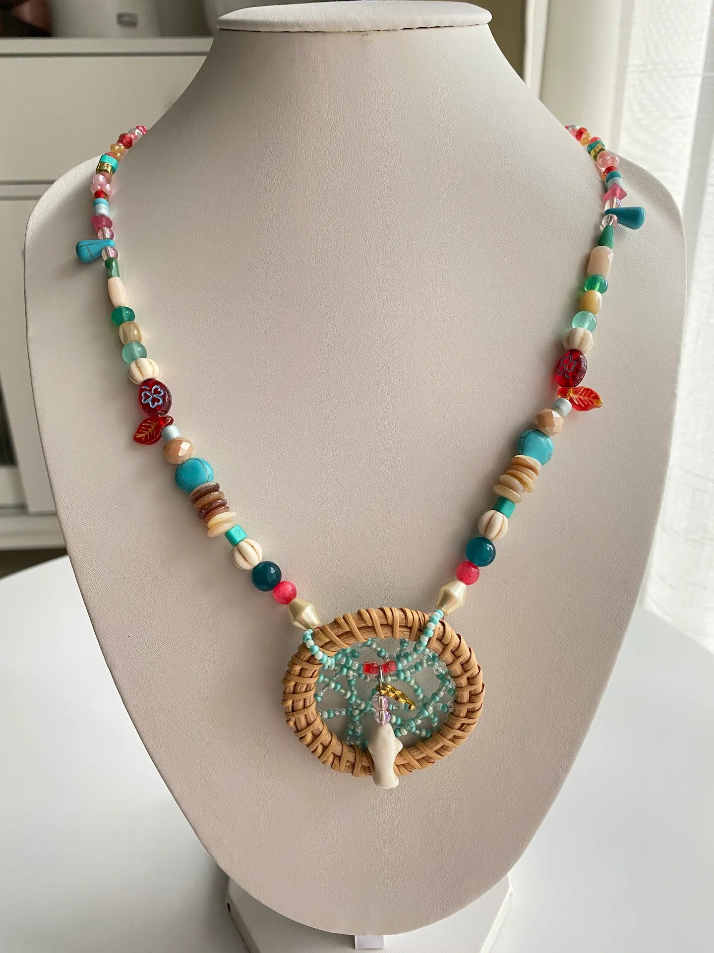A 24.4-inch handcrafted extra-long necklace with a dreamcatcher pendant and a turquoise fish centerpiece on a jewelry bust.