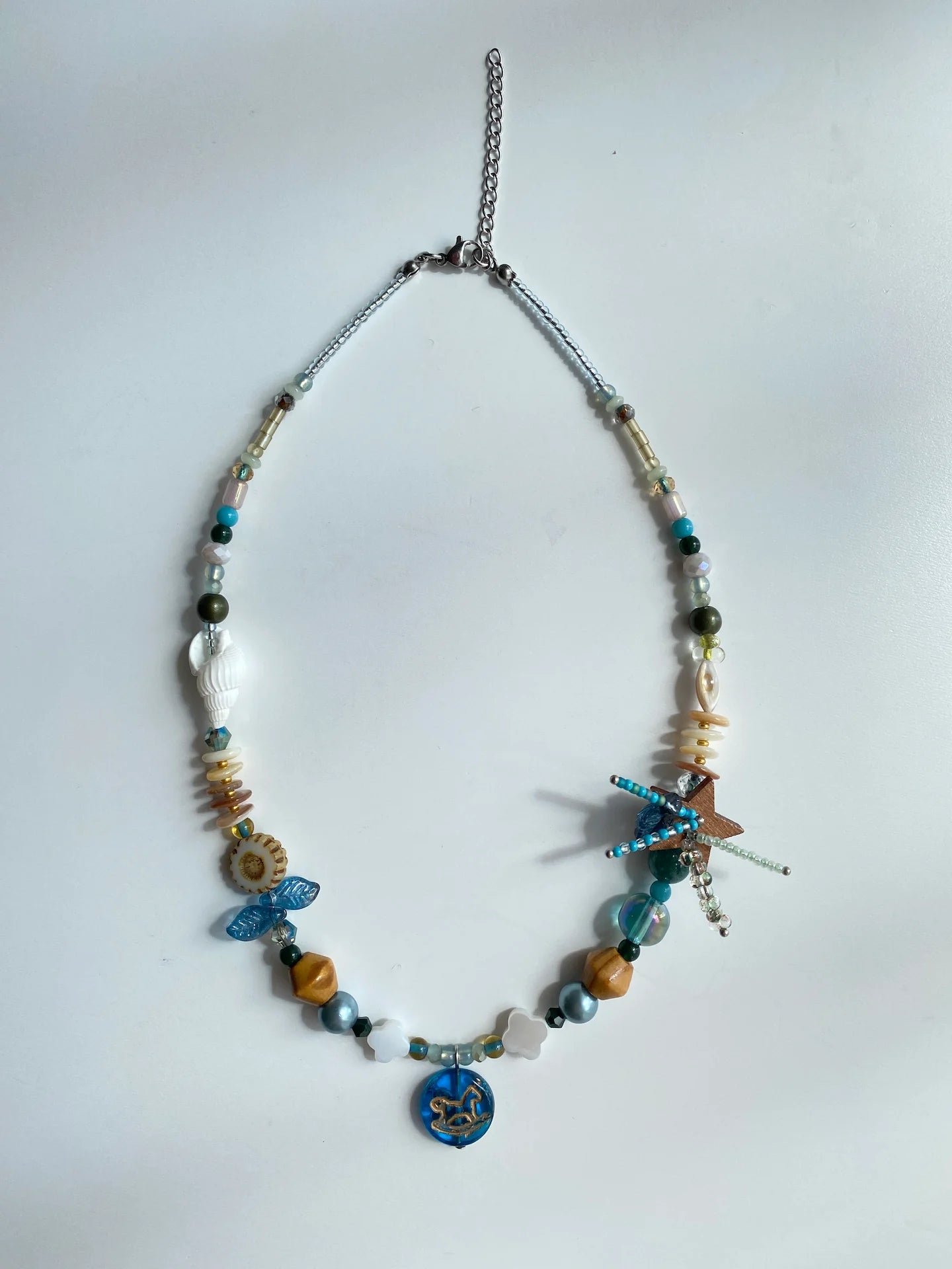 Flat lay of the 1-of-1 handmade necklace on a white table, showing coconut star fireworks and Czech glass horse details.