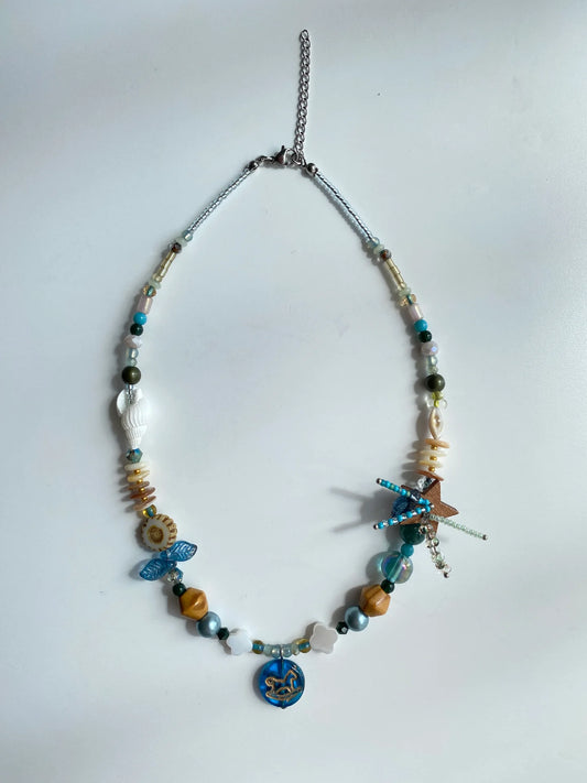 Flat lay of the 1-of-1 handmade necklace on a white table, showing coconut star fireworks and Czech glass horse details.
