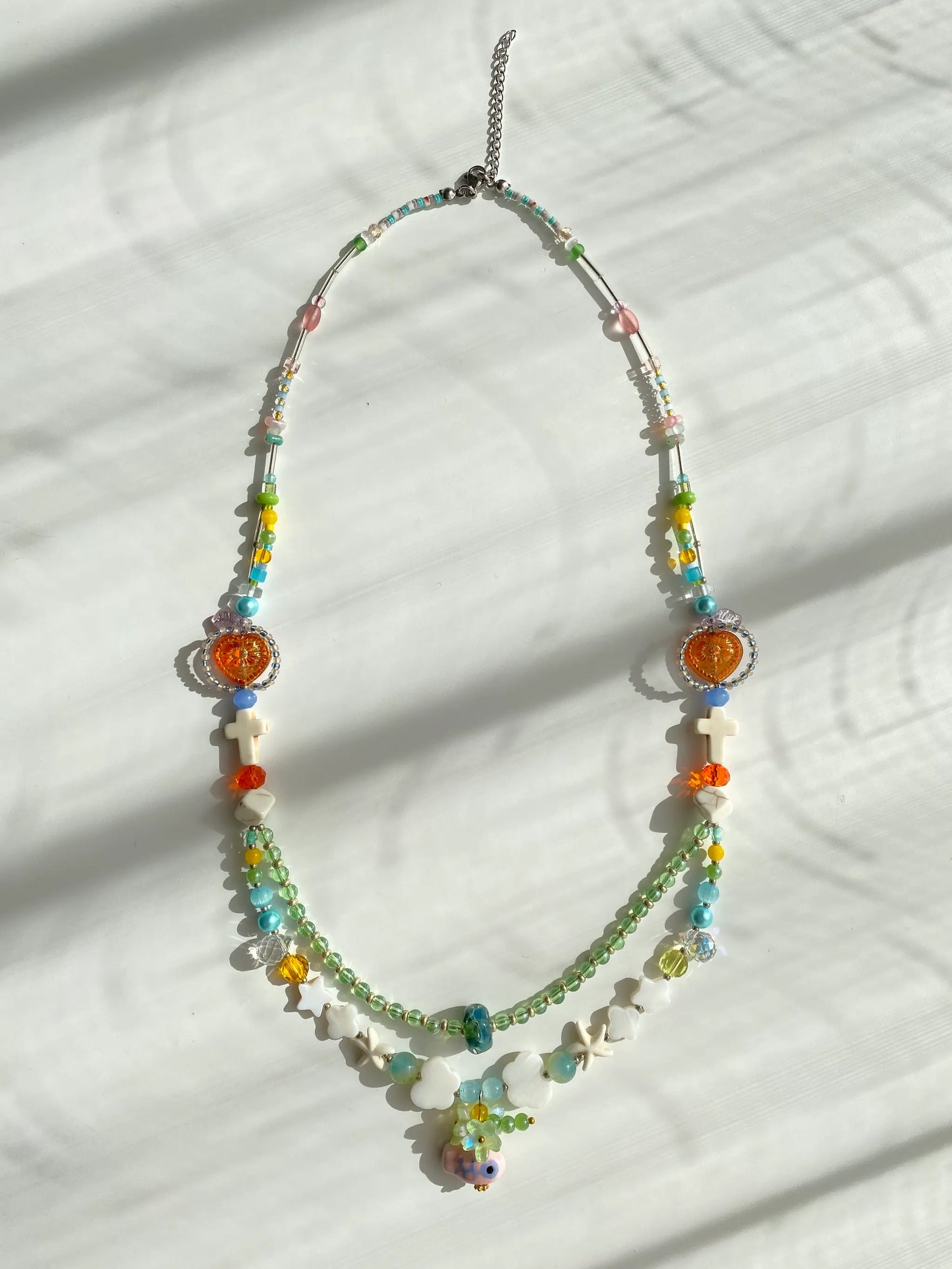 Flat lay of HuibenCraft 1-of-1 necklace on a white table, showing red heart, pink duck pendant, and various bead shapes.