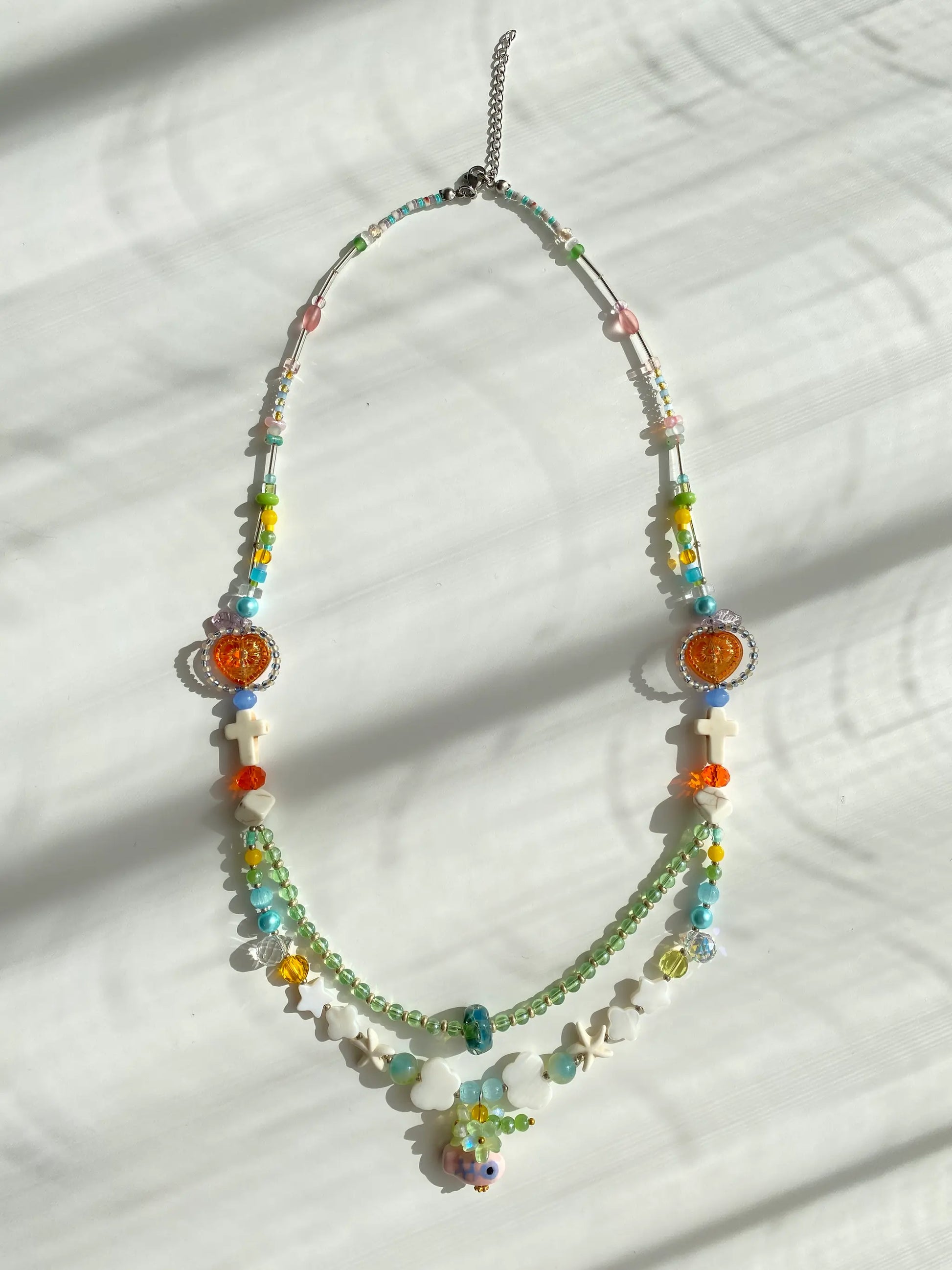 Flat lay of HuibenCraft 1-of-1 necklace on a white table, showing red heart, pink duck pendant, and various bead shapes.