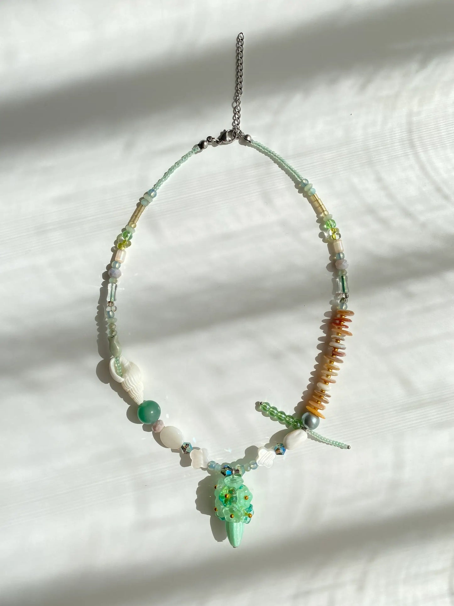 Flat lay of HuibenCraft 1-of-1 necklace on a white table, showing 3D floral bouquet, Czech glass vase, and shell details.