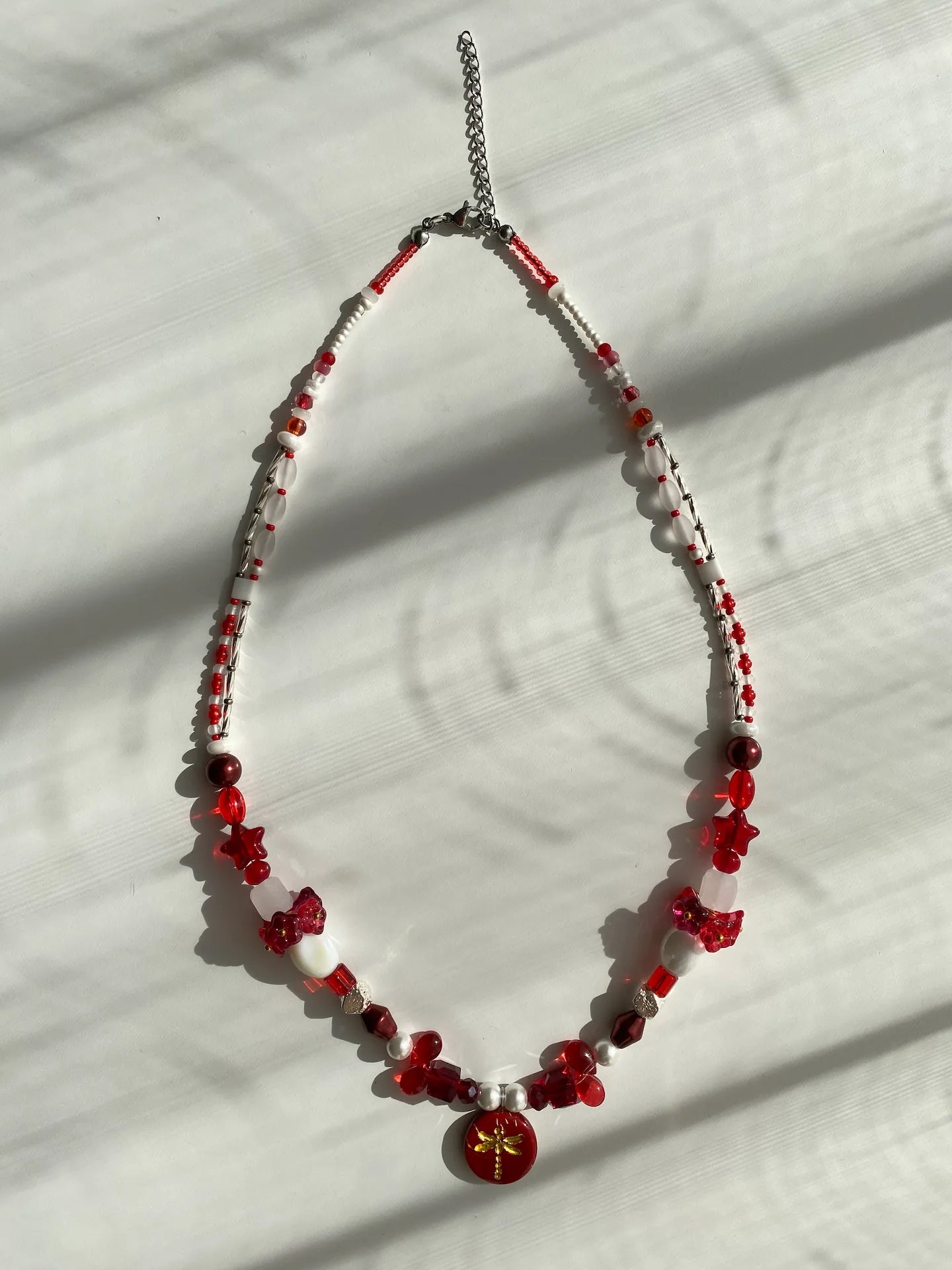 Flat lay of HuibenCraft 1-of-1 necklace on a white table, showing butterfly pendant and floral vase beadwork details.