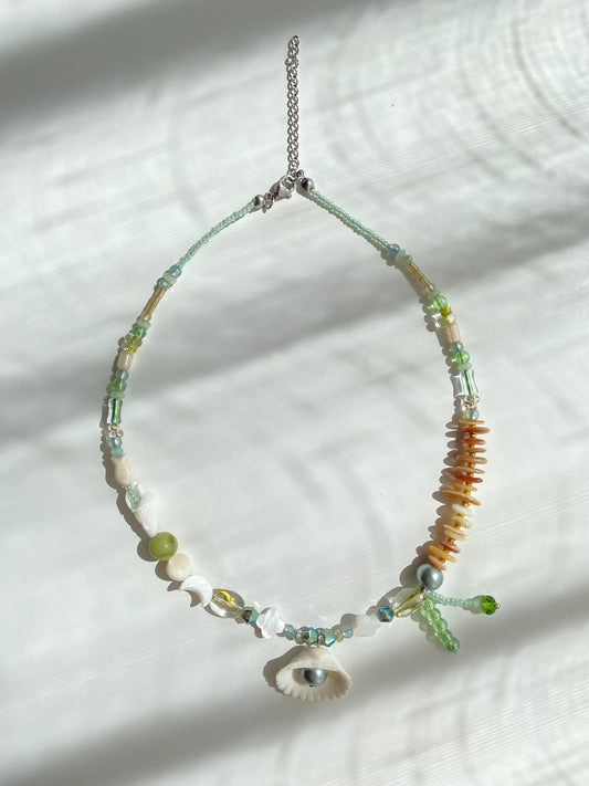 Flat lay shot on a white table of the handcrafted 1-of-1 shell necklace, clearly displaying the conch, fish, clover shell, and pendant details.