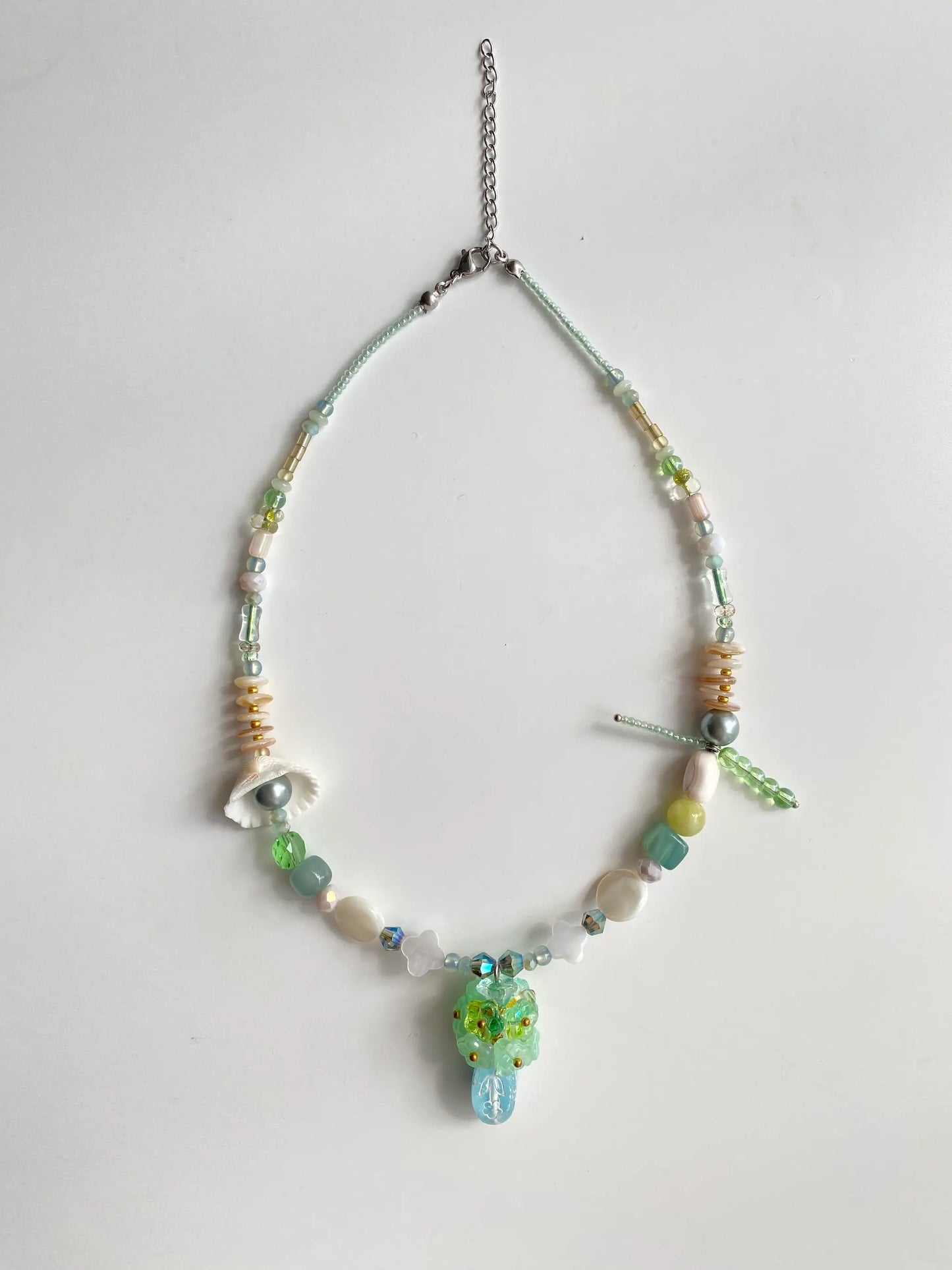 Flat lay of HuibenCraft 1-of-1 necklace on a white table, showing 3D floral bouquet, glass vase, and shell details.