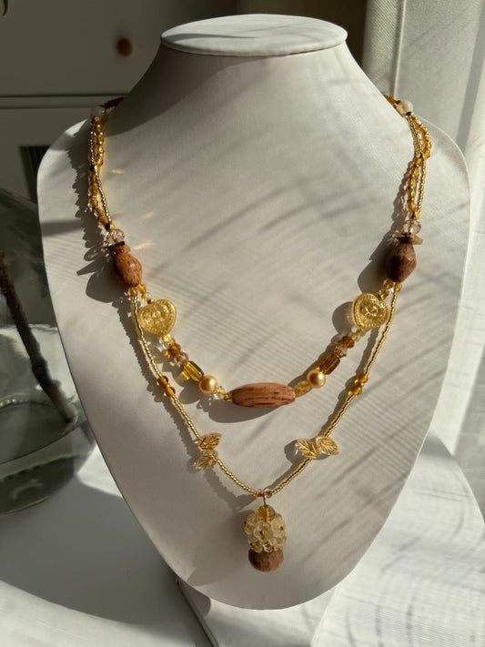 A 1-of-1 heavy workmanship double-layered necklace featuring 9 handcrafted glass flowers blooming from a wooden vase pendant on a jewelry bust.