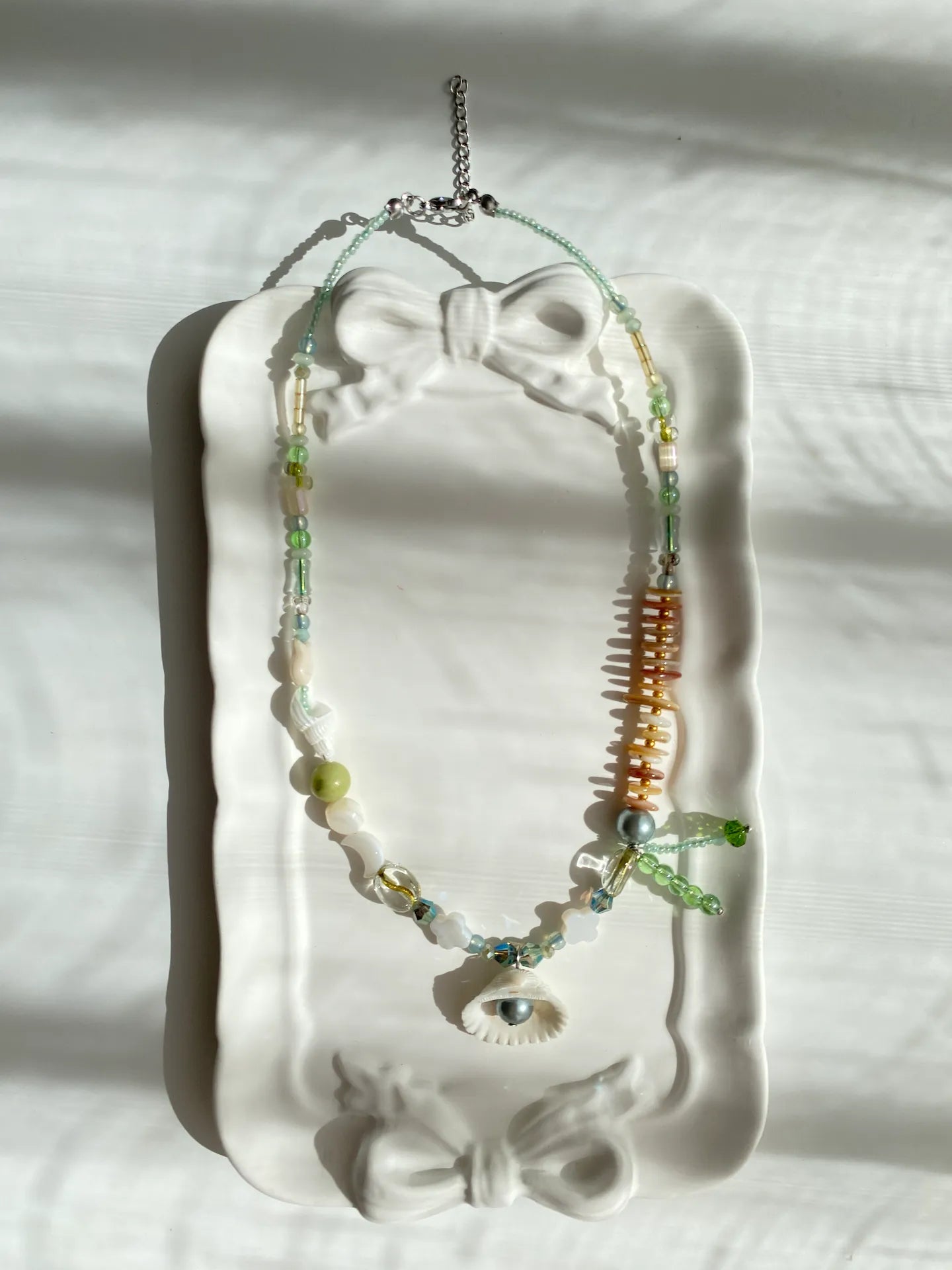 A poetic photo of the 1-of-1 ocean aesthetic necklace resting on a ceramic plate, capturing a nostalgic beach vibe.