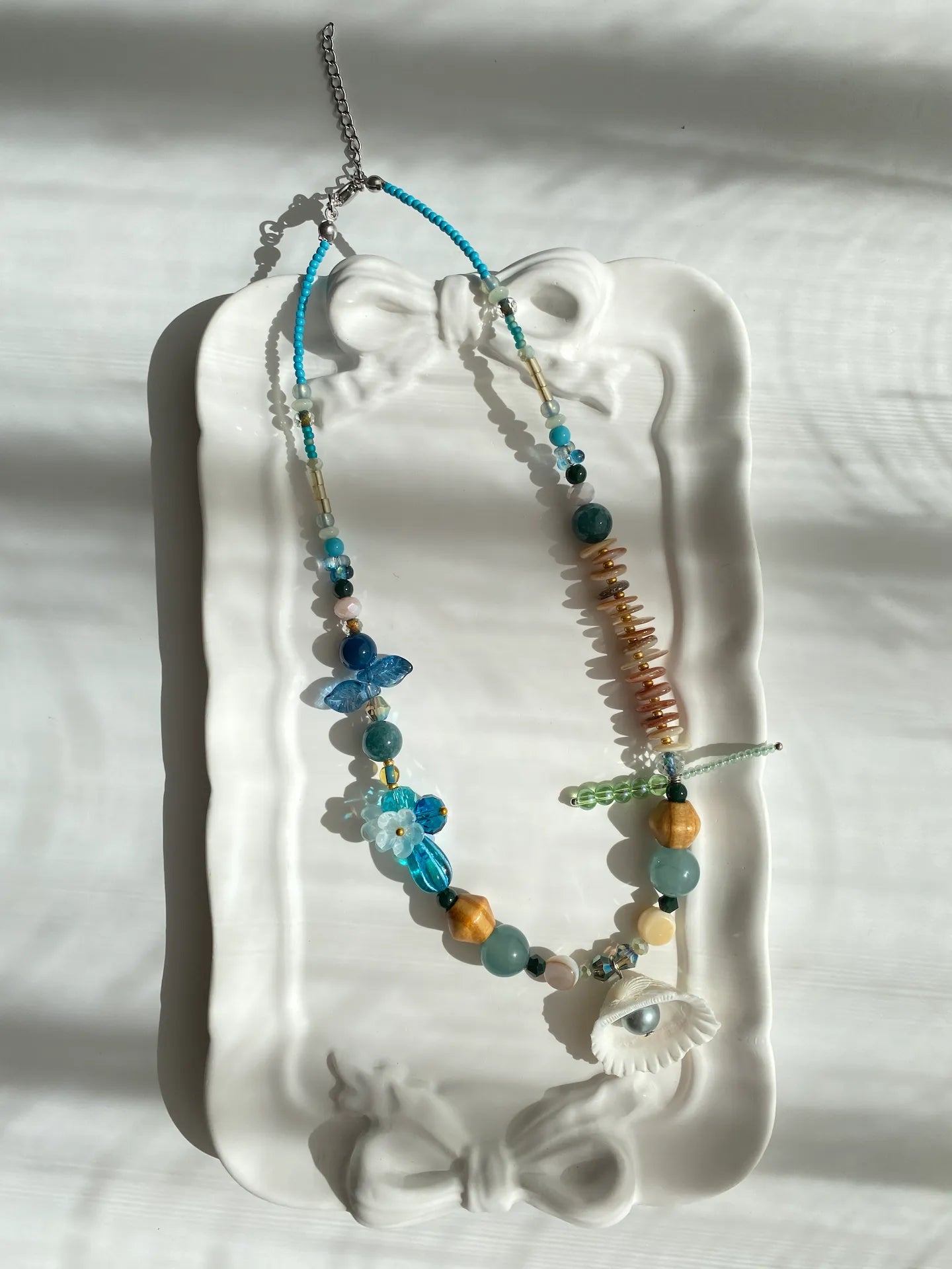 A poetic photo of the 1-of-1 ocean-style necklace resting on a ceramic plate, capturing a nostalgic beach aesthetic.