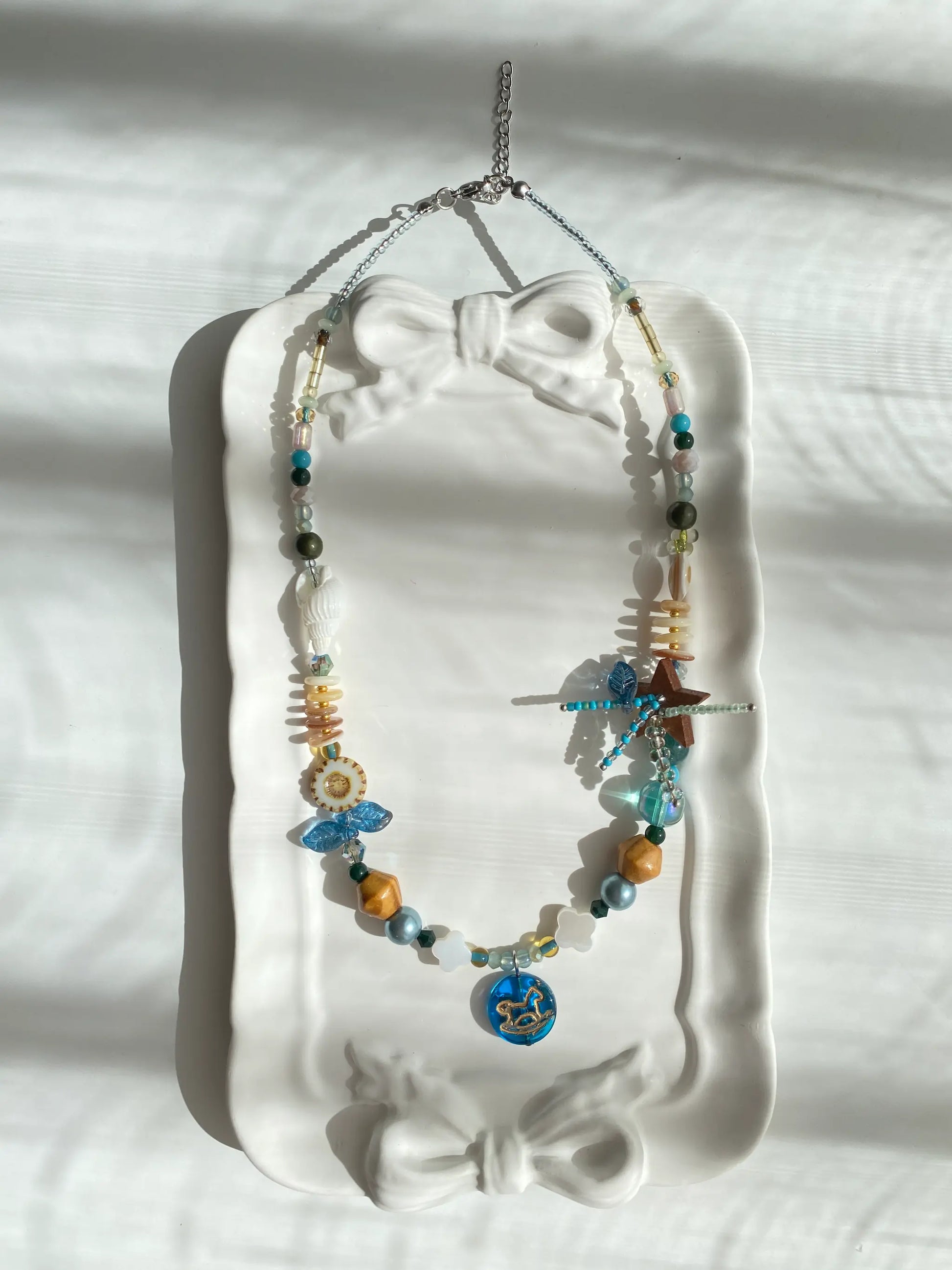 Poetic view of the 1-of-1 blue star and horse necklace resting on a ceramic plate, capturing a playful and cute aesthetic.