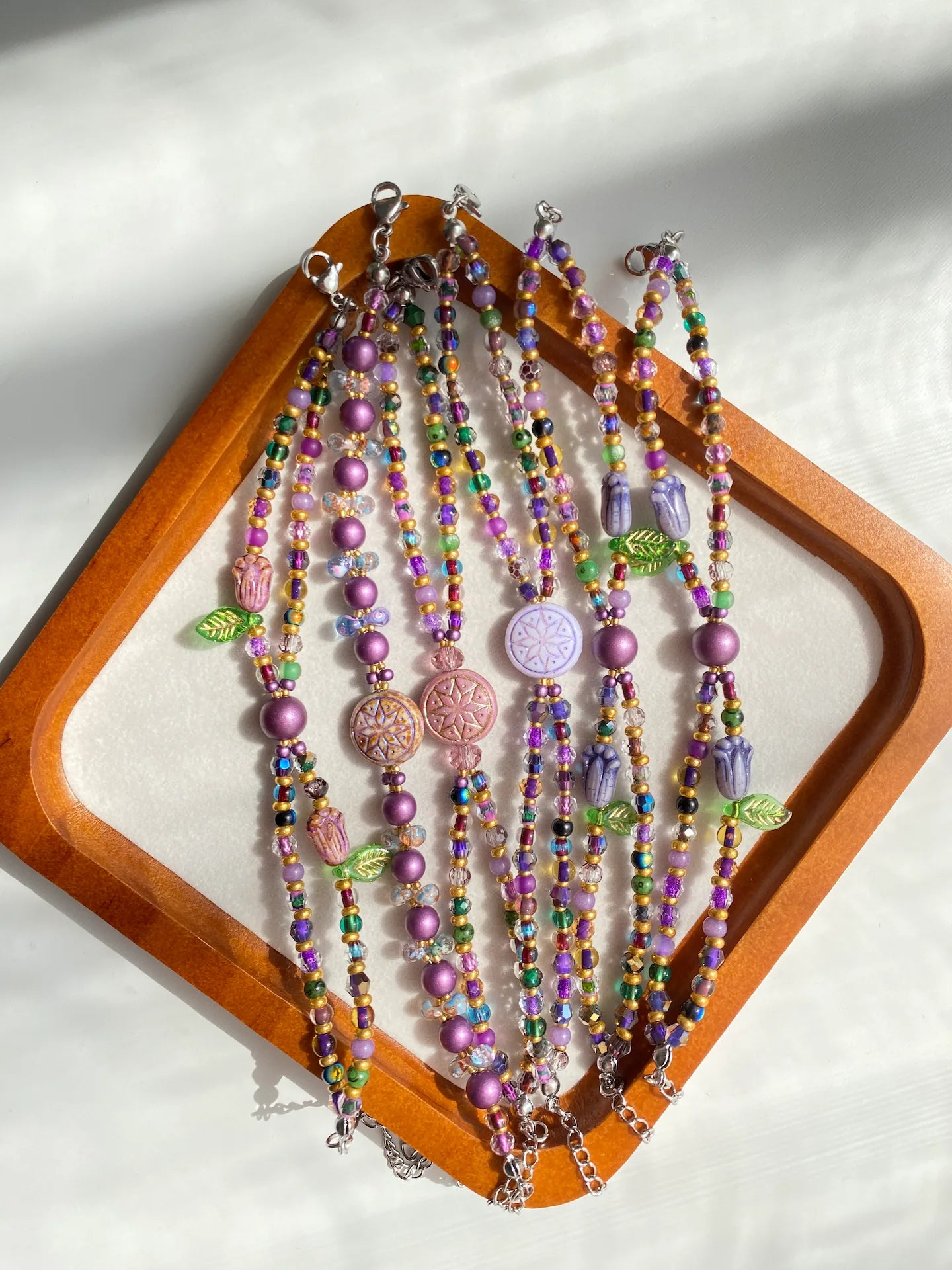 Six HuibenCraft 1-of-1 purple and gold double-layered bracelets displayed in a wooden tray under natural sunlight.