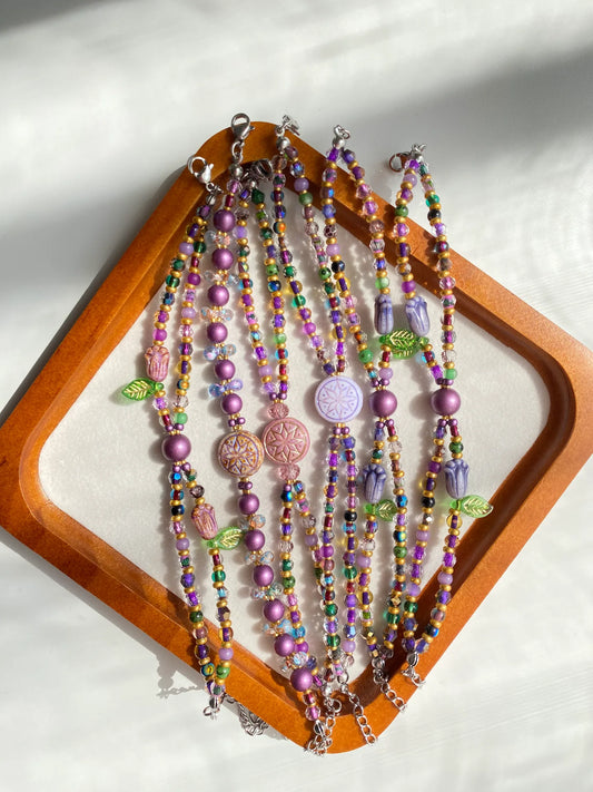 Six HuibenCraft 1-of-1 purple and gold double-layered bracelets displayed in a wooden tray under natural sunlight.