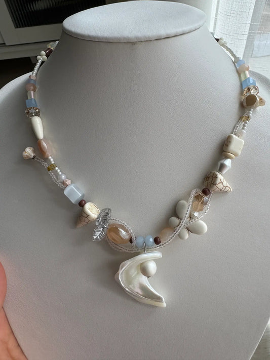 A 1-of-1 sacred-style necklace with a large trochus shell pendant cradling a milky white bead on a jewelry bust, sky blue and sandy tones.