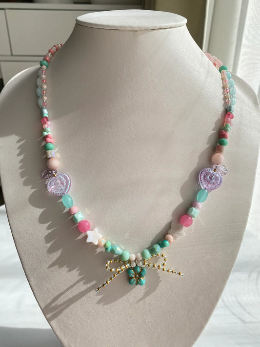 A 1-of-1 lively beaded necklace in sky blue and pink with a starfish-shaped Czech glass pendant and a handmade seed bead bow on a jewelry bust.