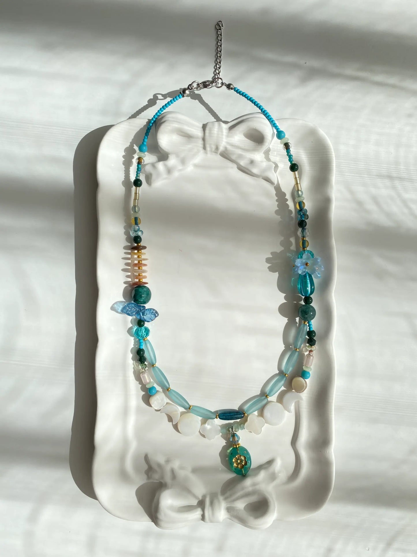 Poetic view of the 1-of-1 heavy-duty necklace with perfume bottle pendant resting on a ceramic plate, capturing a luxurious aesthetic.