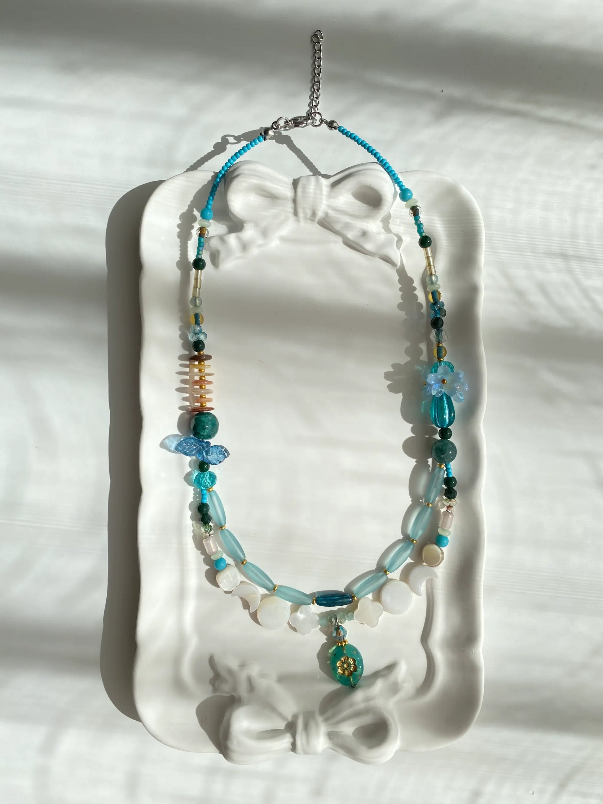 Poetic view of the 1-of-1 heavy-duty necklace with perfume bottle pendant resting on a ceramic plate, capturing a luxurious aesthetic.
