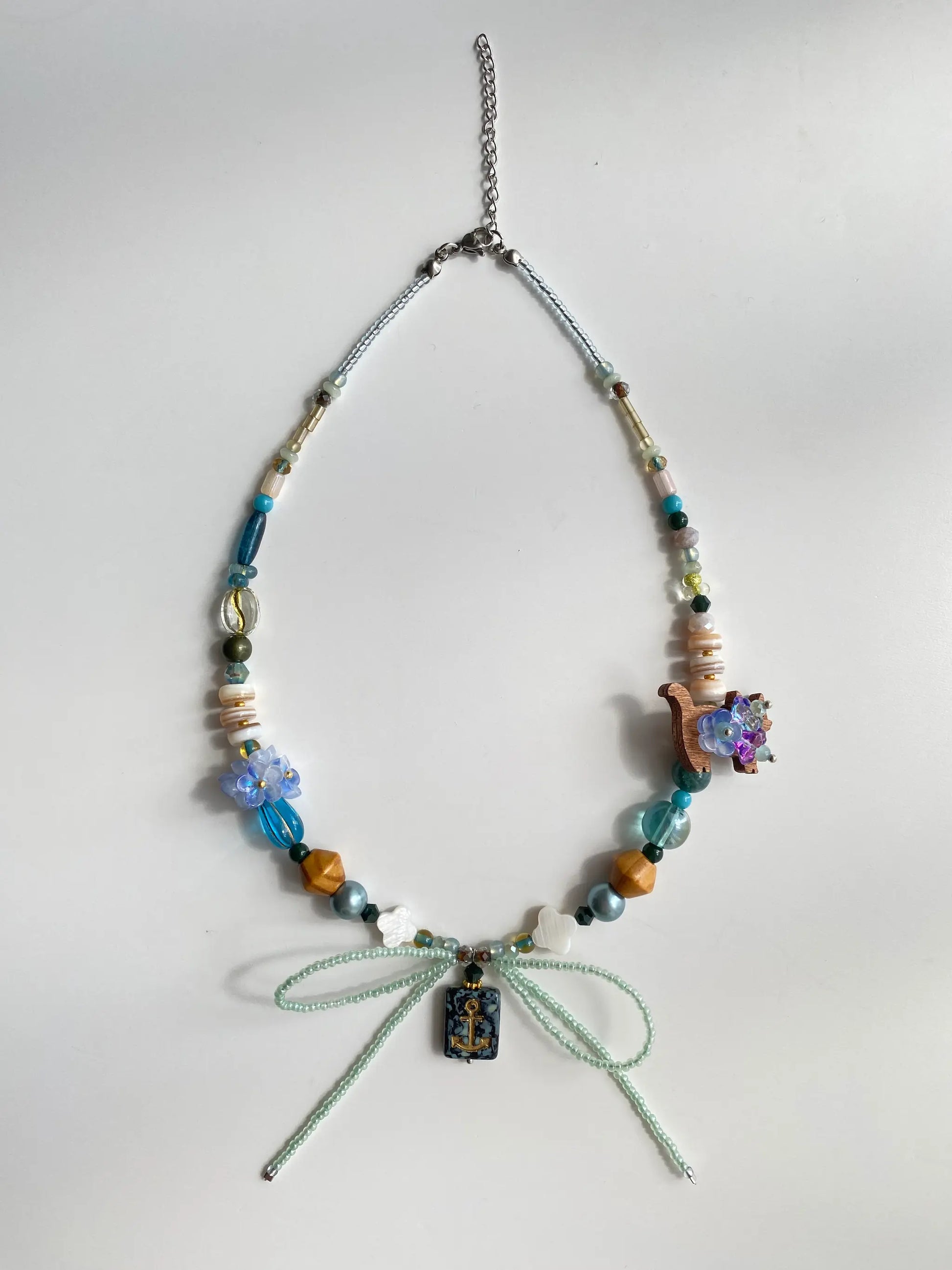 Flat lay of HuibenCraft 1-of-1 necklace on a white table, showing Cancer pendant, coconut cat, and clover shell details.