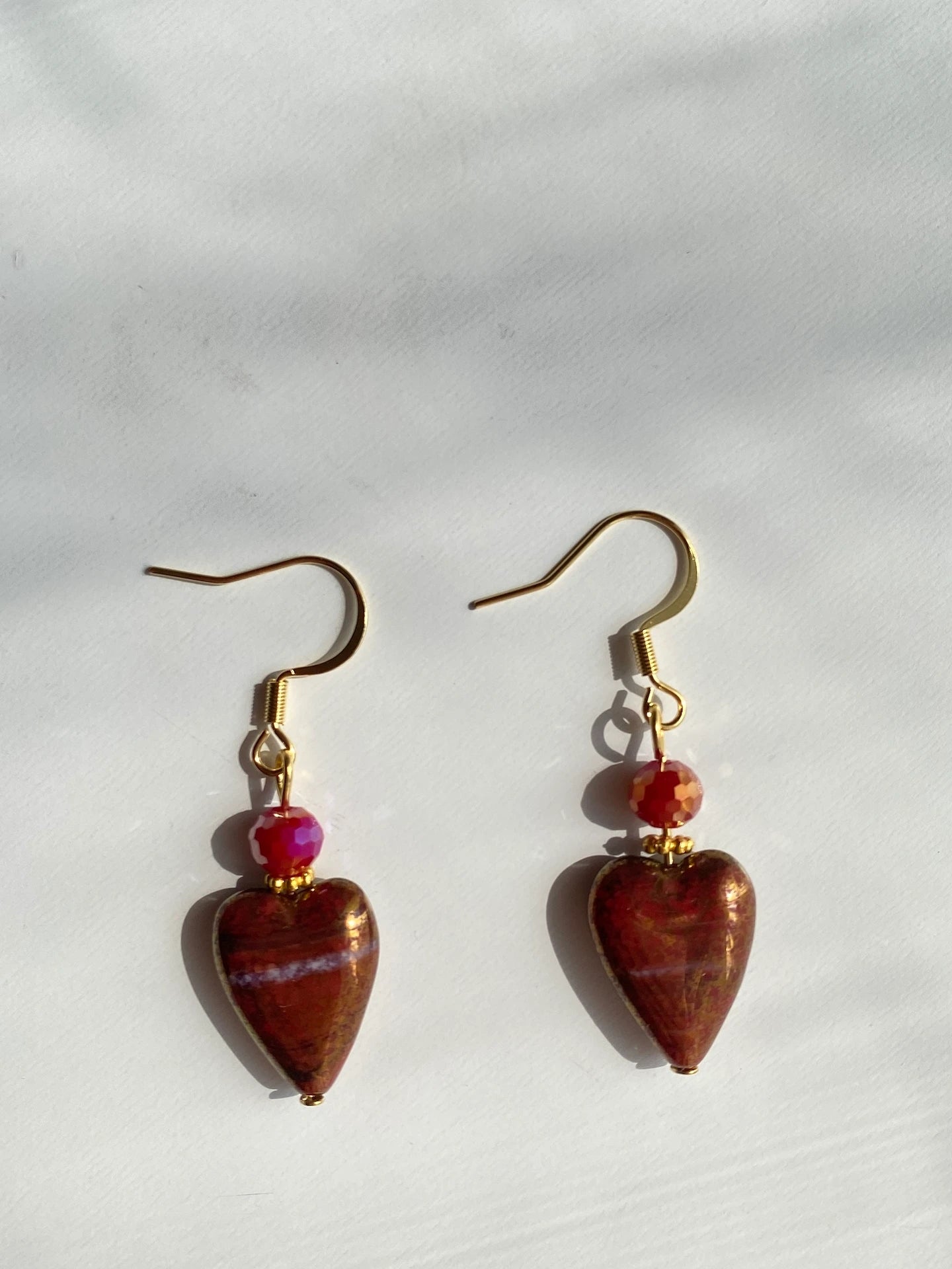 A 1-of-1 pair of 80s vintage-style earrings with red gold-rimmed Czech glass hearts and sparkling faceted red beads on a desk.