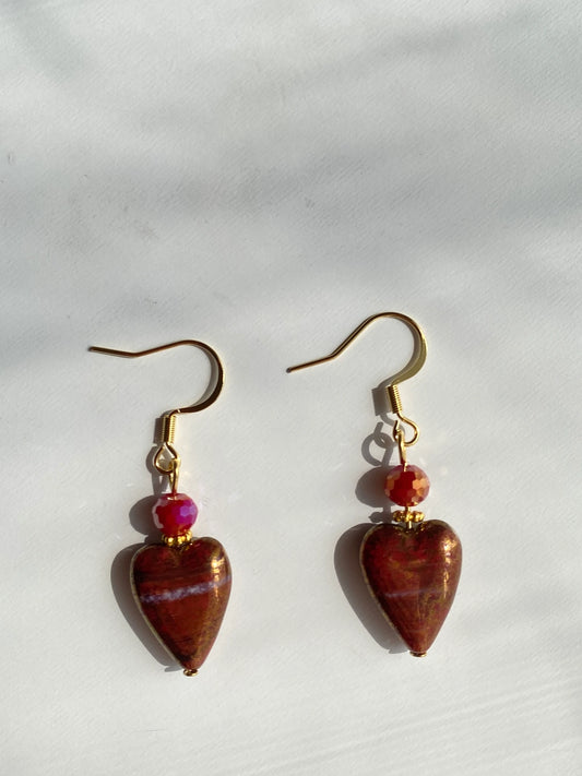 A 1-of-1 pair of 80s vintage-style earrings with red gold-rimmed Czech glass hearts and sparkling faceted red beads on a desk.