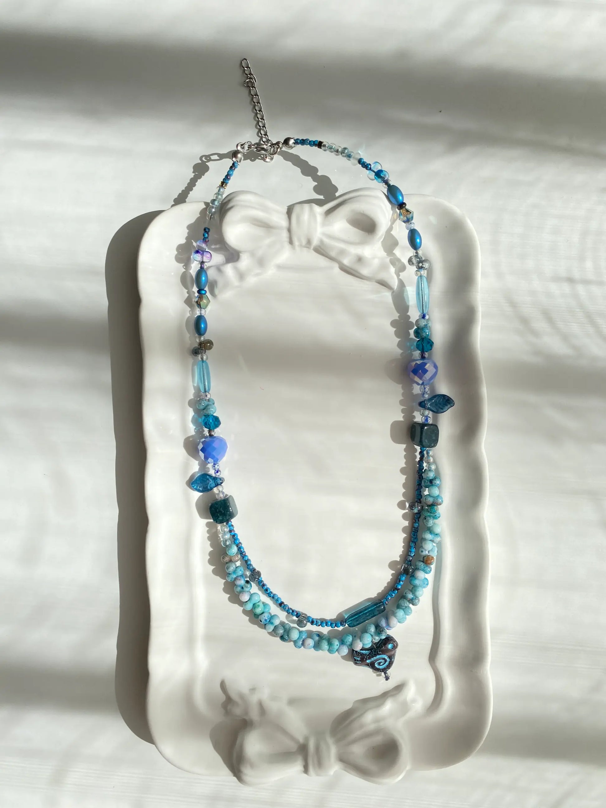 Poetic view of the 1-of-1 vintage-style layered necklace resting on a ceramic plate, capturing an antique aesthetic.