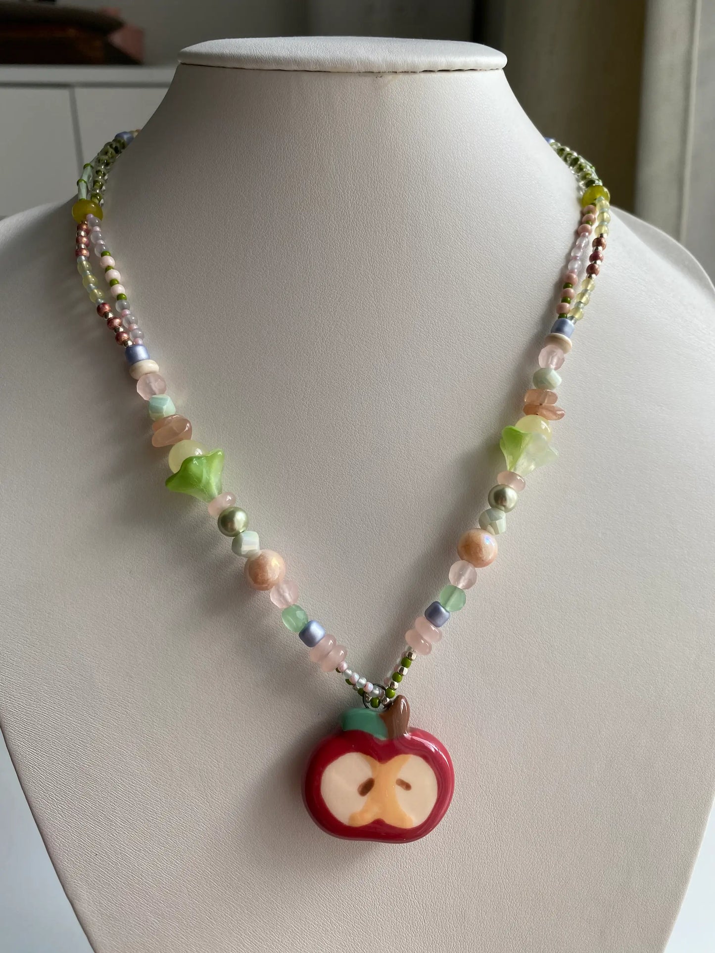 A model wearing a handcrafted HuibenCraft beaded necklace with a red ceramic apple pendant.