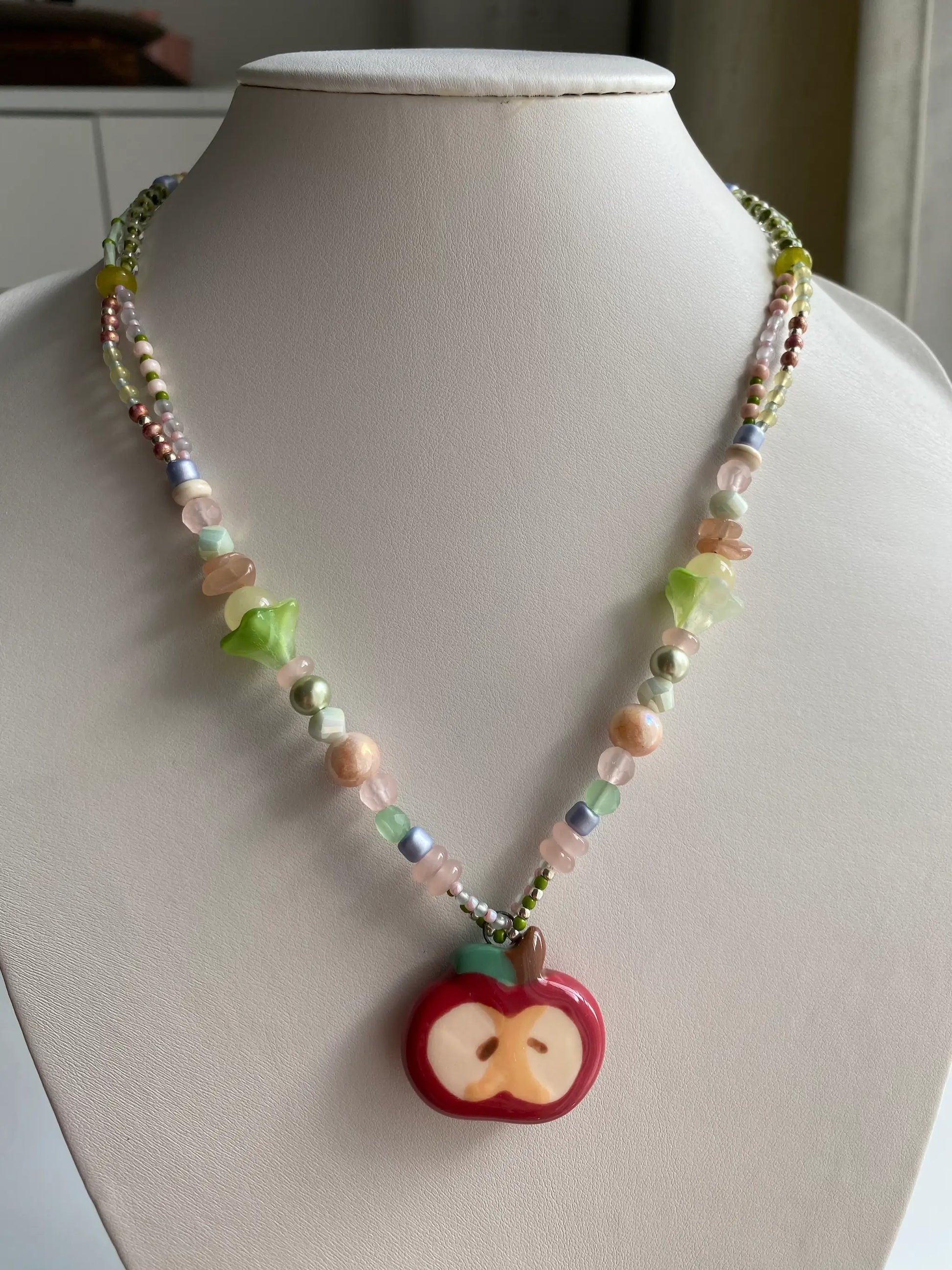 A model wearing a handcrafted HuibenCraft beaded necklace with a red ceramic apple pendant.
