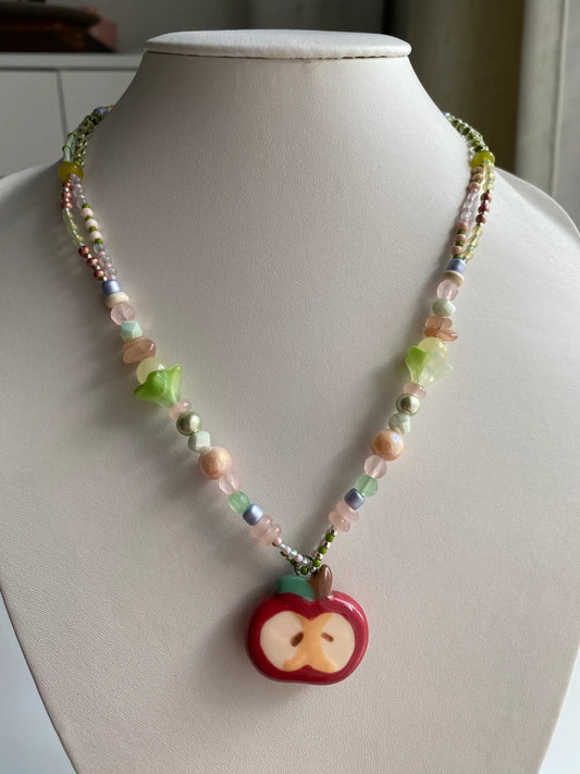 A model wearing a handcrafted HuibenCraft beaded necklace with a red ceramic apple pendant.