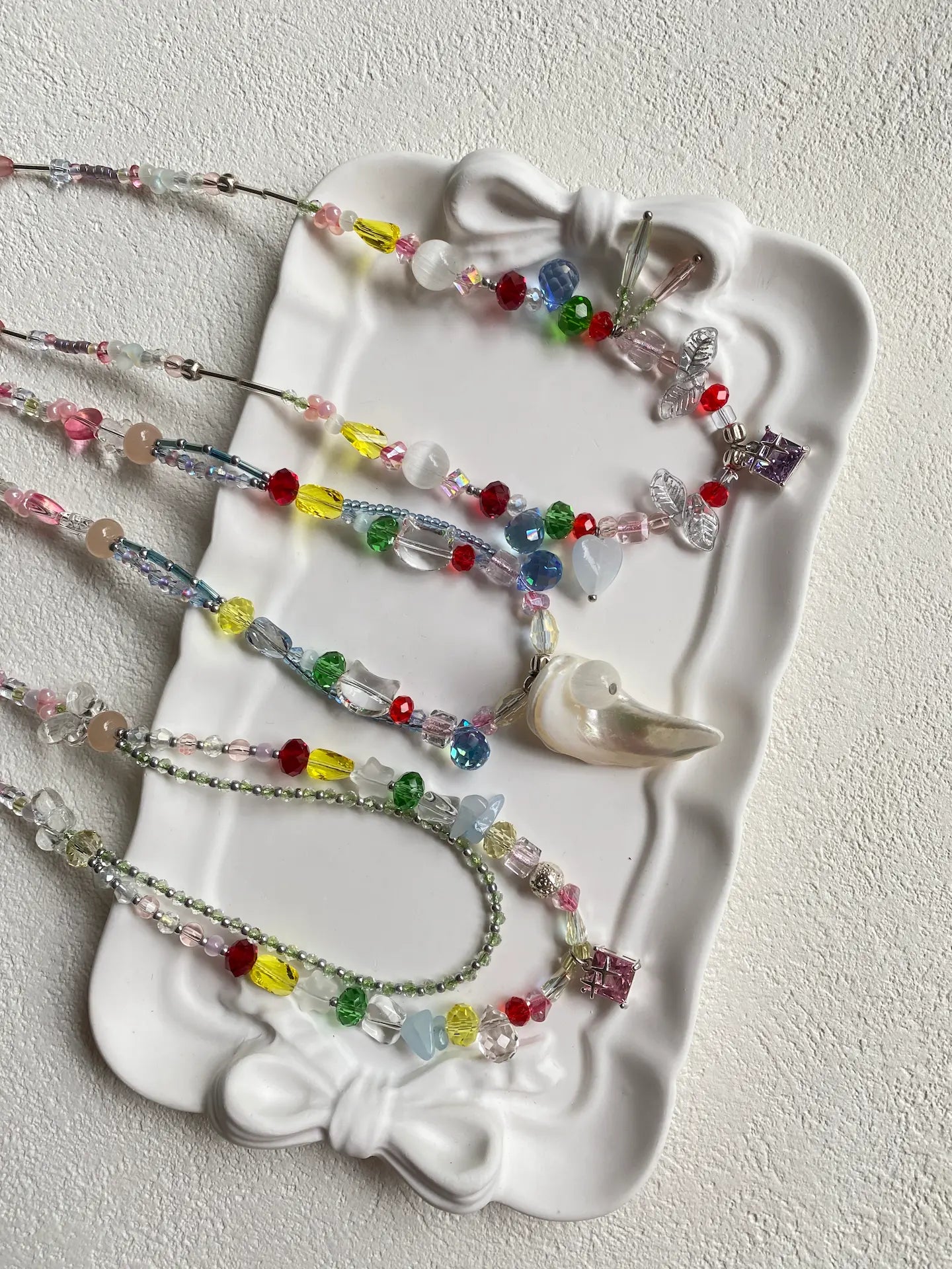 Detailed top-down shot of three unique HuibenCraft vibrant mixed-color seed bead necklaces glittering together in a dish.