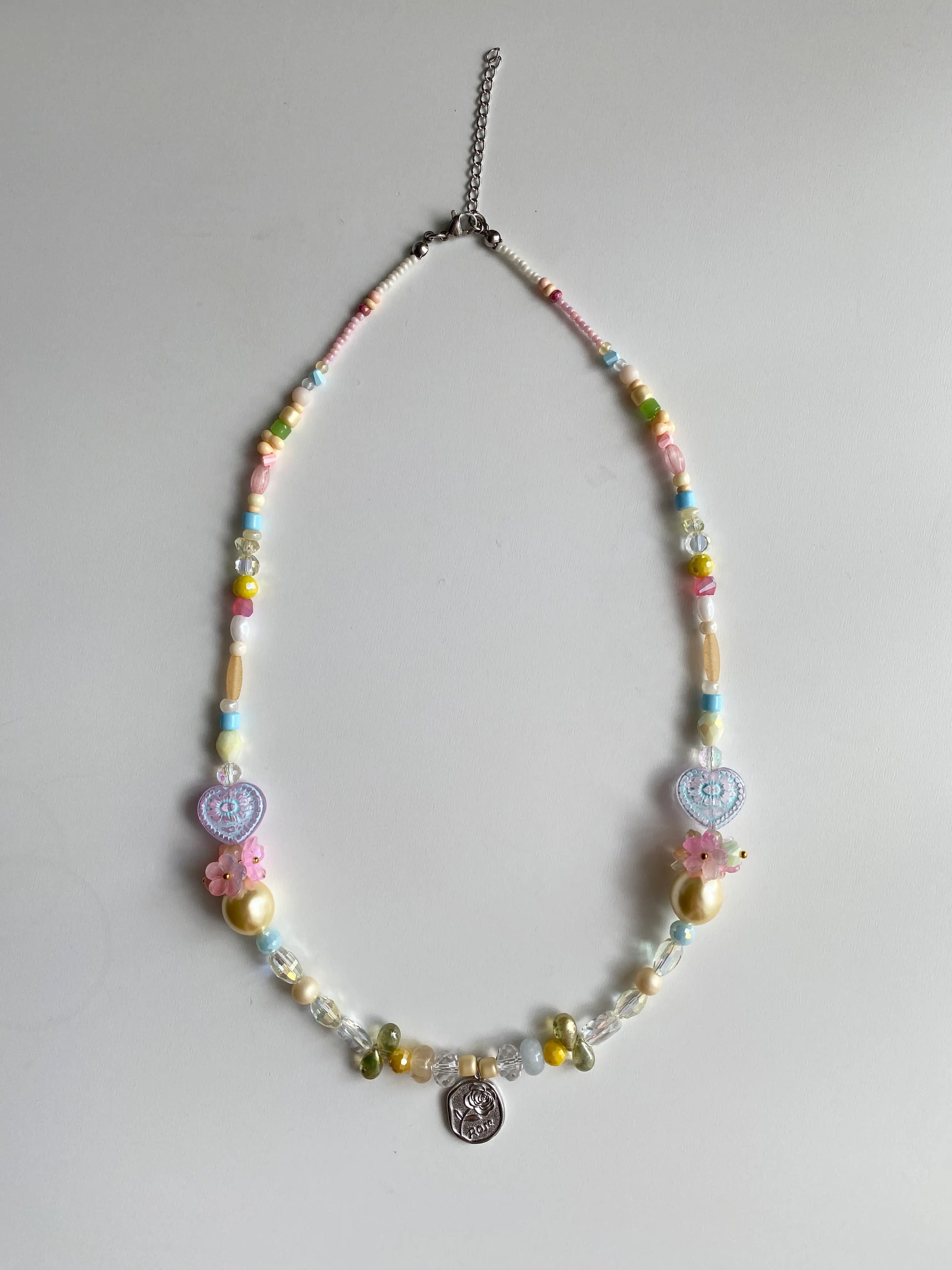 Flatlay of a symmetric garden-themed necklace featuring twin flower bouquets and heart-shaped glass beads.