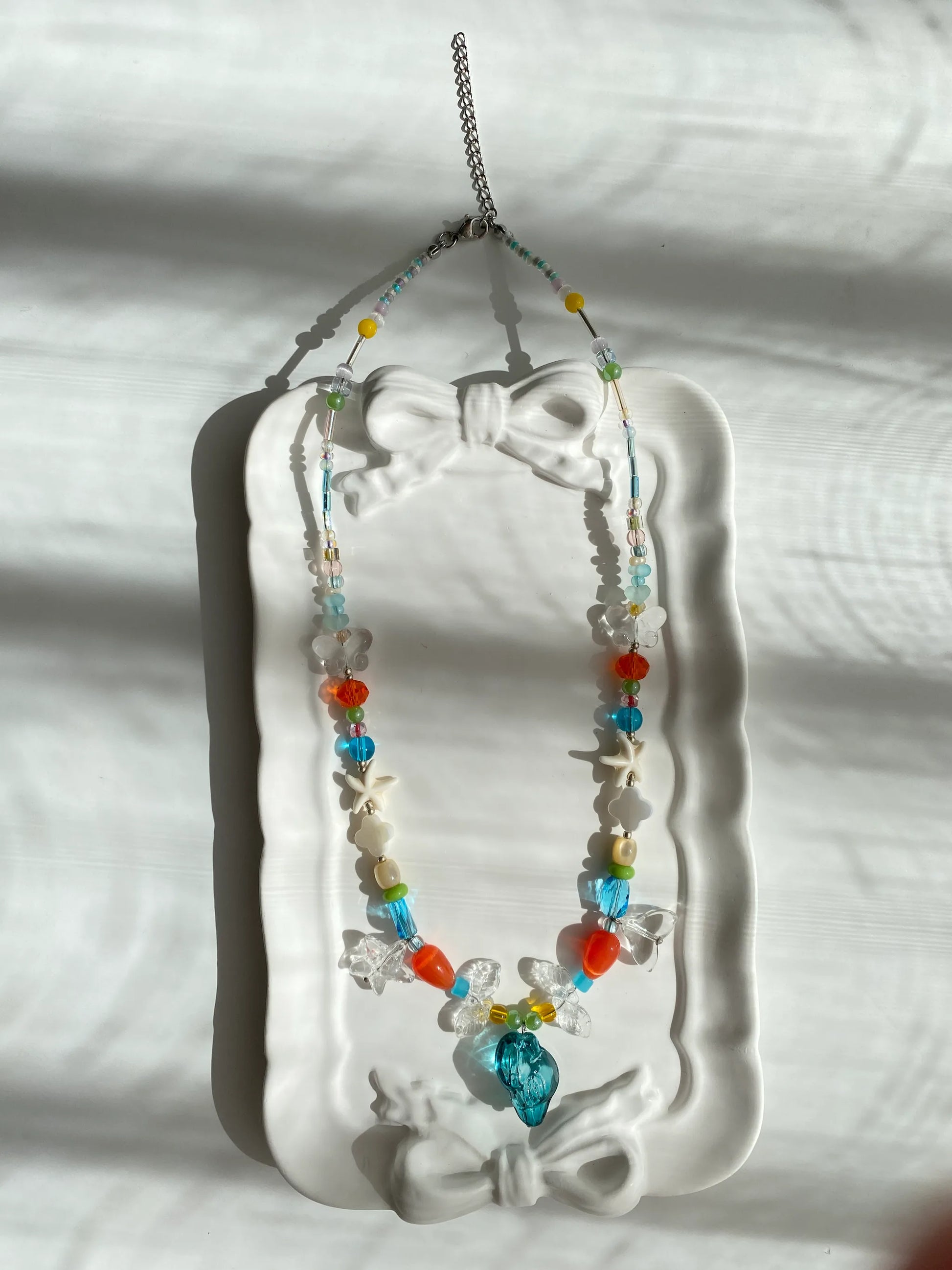A top-down look at the conch and fishtail beaded necklace in a ceramic dish, emphasizing its cool ocean colors.