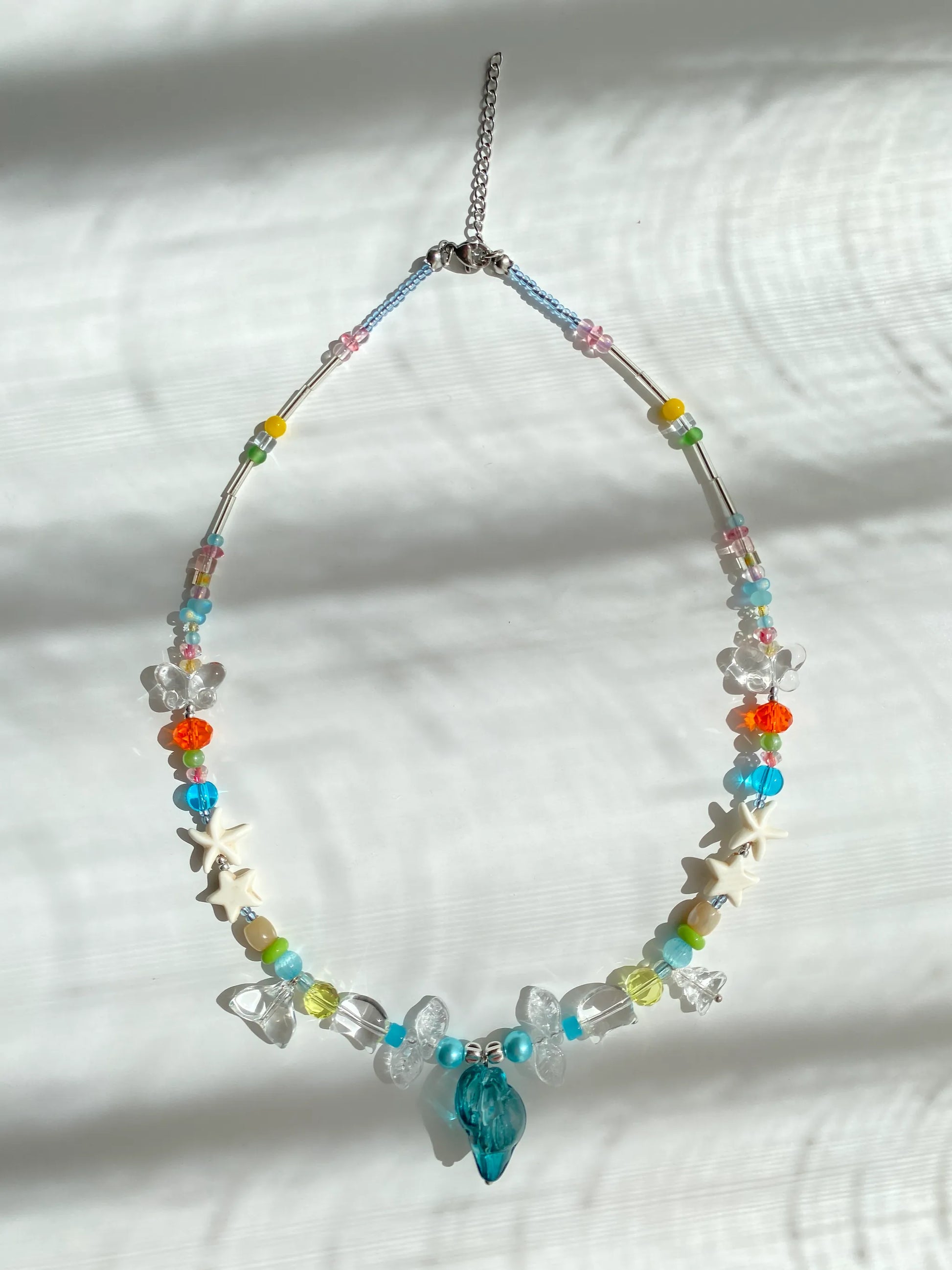 Translucent blue conch and glass kitty beads catching the sun, creating a refreshing and clear summer vibe.