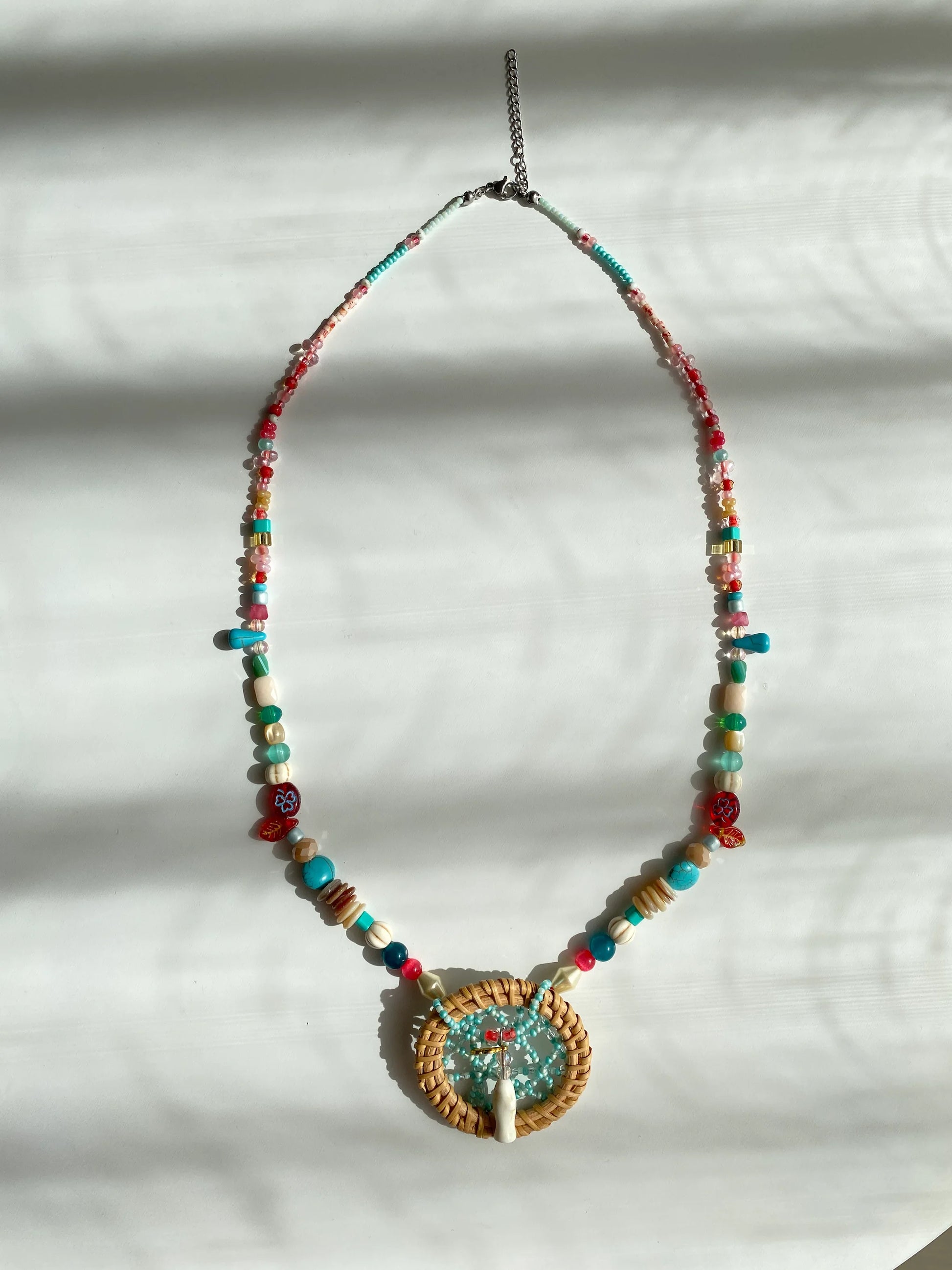Full view of an artisanal mixed-bead necklace featuring over 10 types of beads, including turquoise, shells, and Czech glass clovers on a white desk.